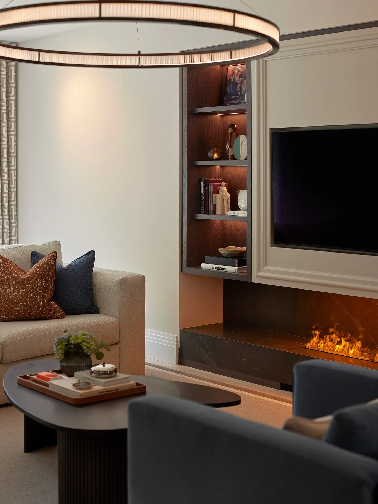 At The Beeches, the formal lounge is anchored by a carefully considered media wall.

The full-width stone fire brings depth and presence, balanced by a painted panelled TV section and bespoke dark-stained oak shelving that adds warmth and symmetry to