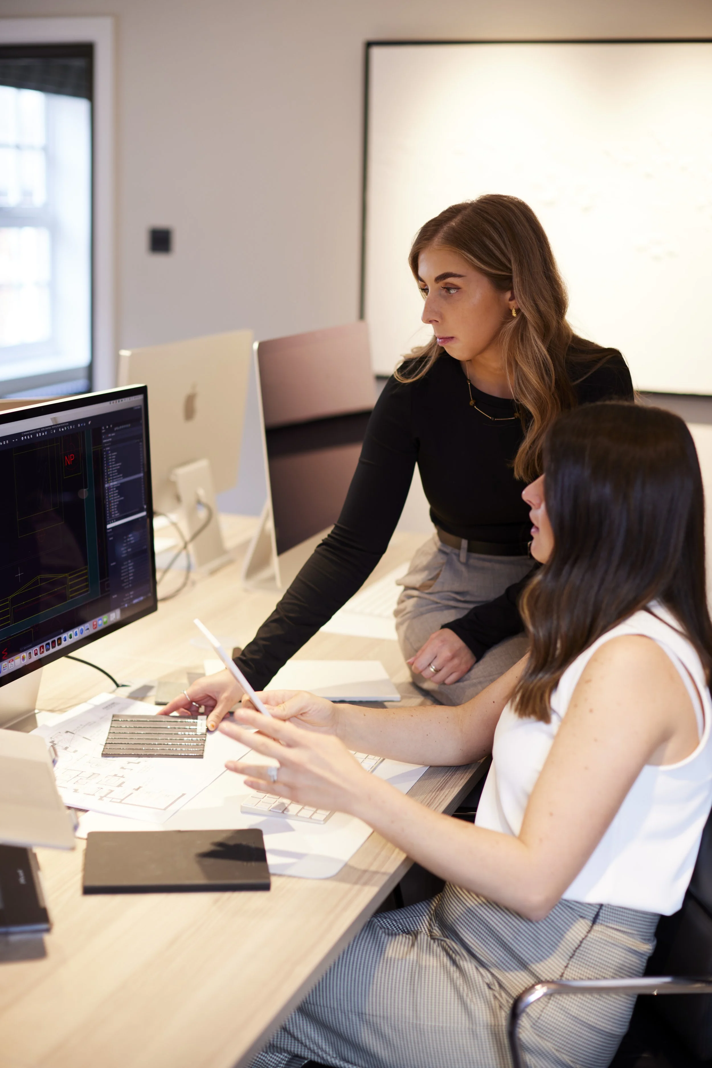 Two women working together in an office, looking at a computer screen, discussing work.