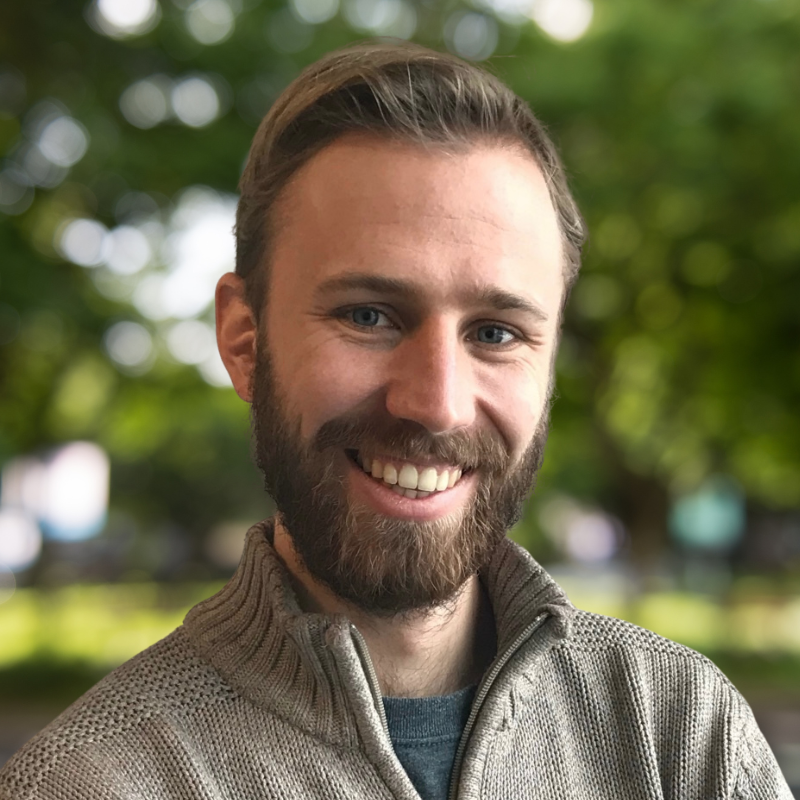 Man with short light brown hair and a beard. He has a smile. He is wearing a light brown sweater.