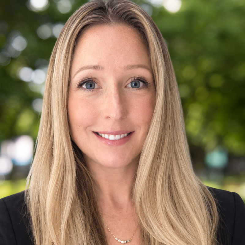 Woman with long blonde hair. Smiling and wearing a black blazer.