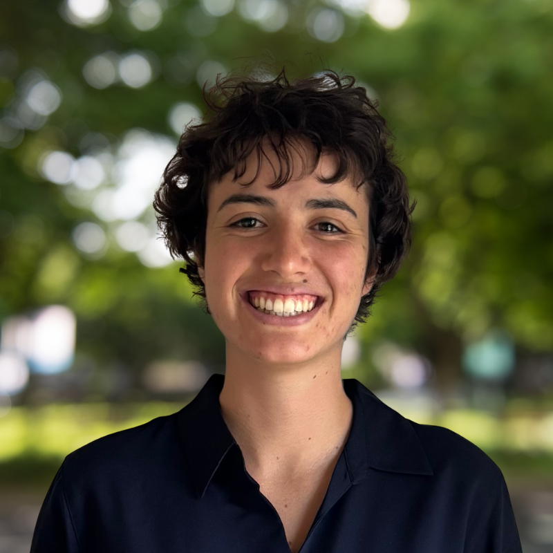 Woman with short curly dark brown hair. She is smiling and wearing a black shirt with a colar.
