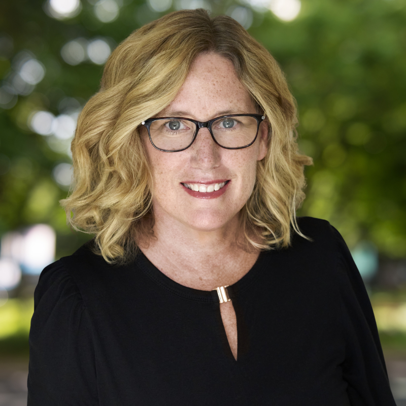Woman with shoulder length curly blonde hair. She is smiling and wearing a black shirt.