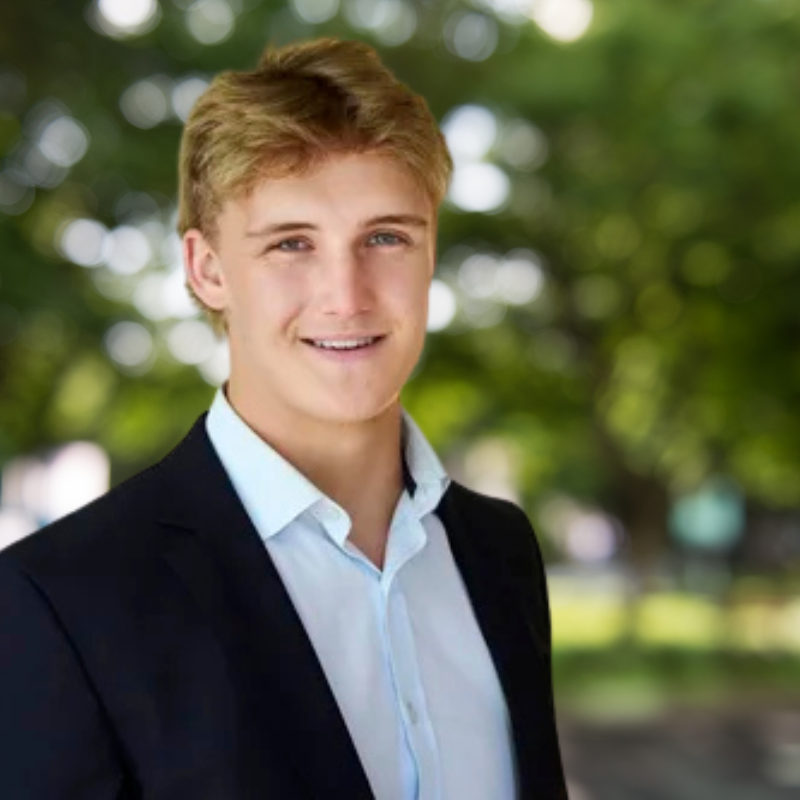 Man with short blonde hair. He is smiling and wearing a black jacket with a white dress shirt underneath.
