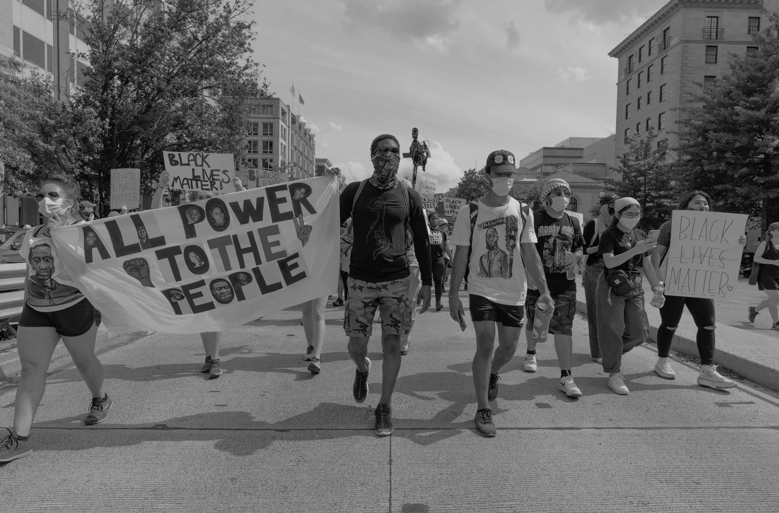 Manifestation pour le mouvement Black Lives Matter avec plusieurs personnes portant des pancartes et des masques, marchant dans une rue en milieu urbain.