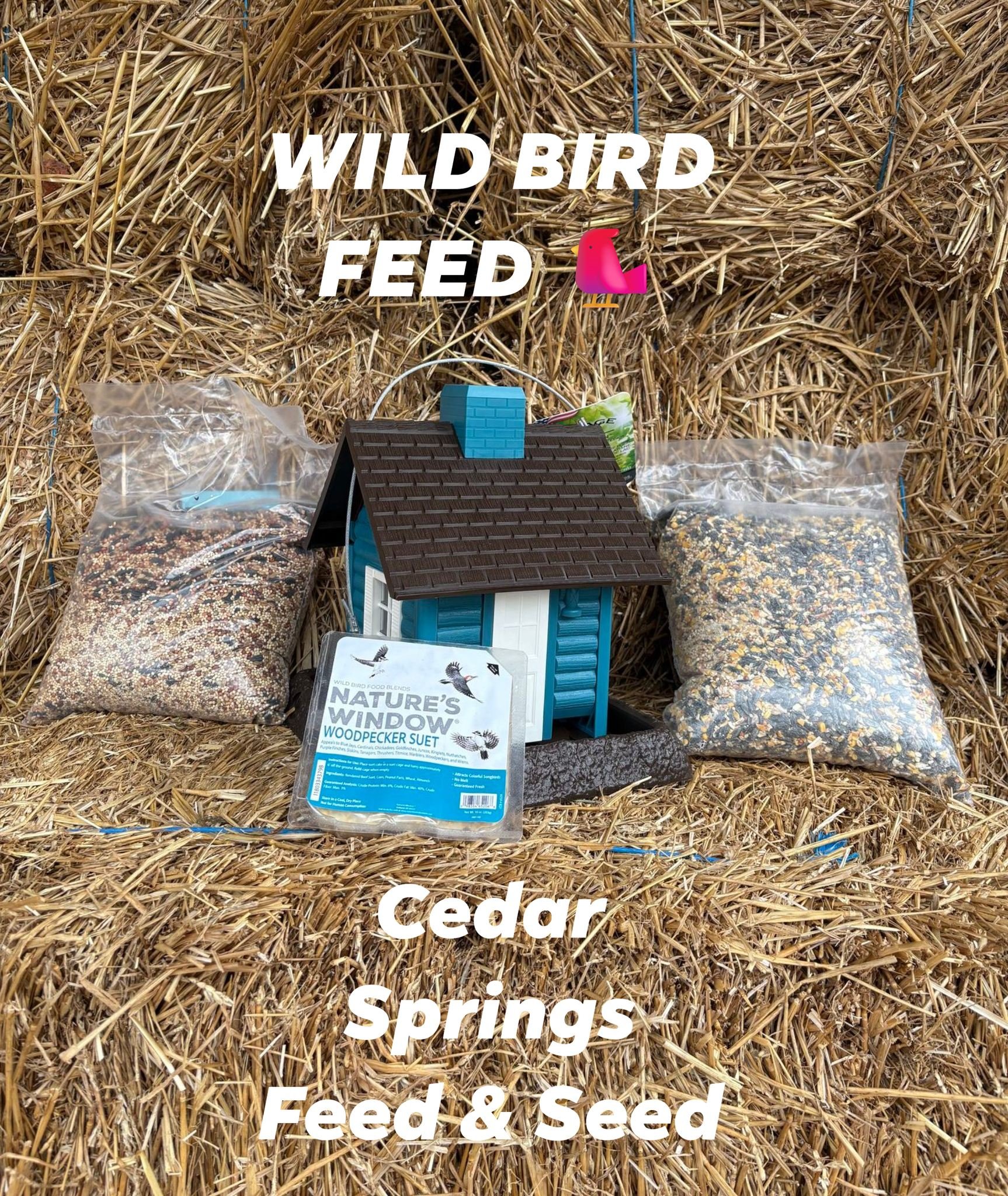 A birdhouse surrounded by bags of bird seed and cedar spring feed, arranged on a pile of hay with text overlay that says "Wild Bird Feed" and "Cedar Springs Feed & Seed."