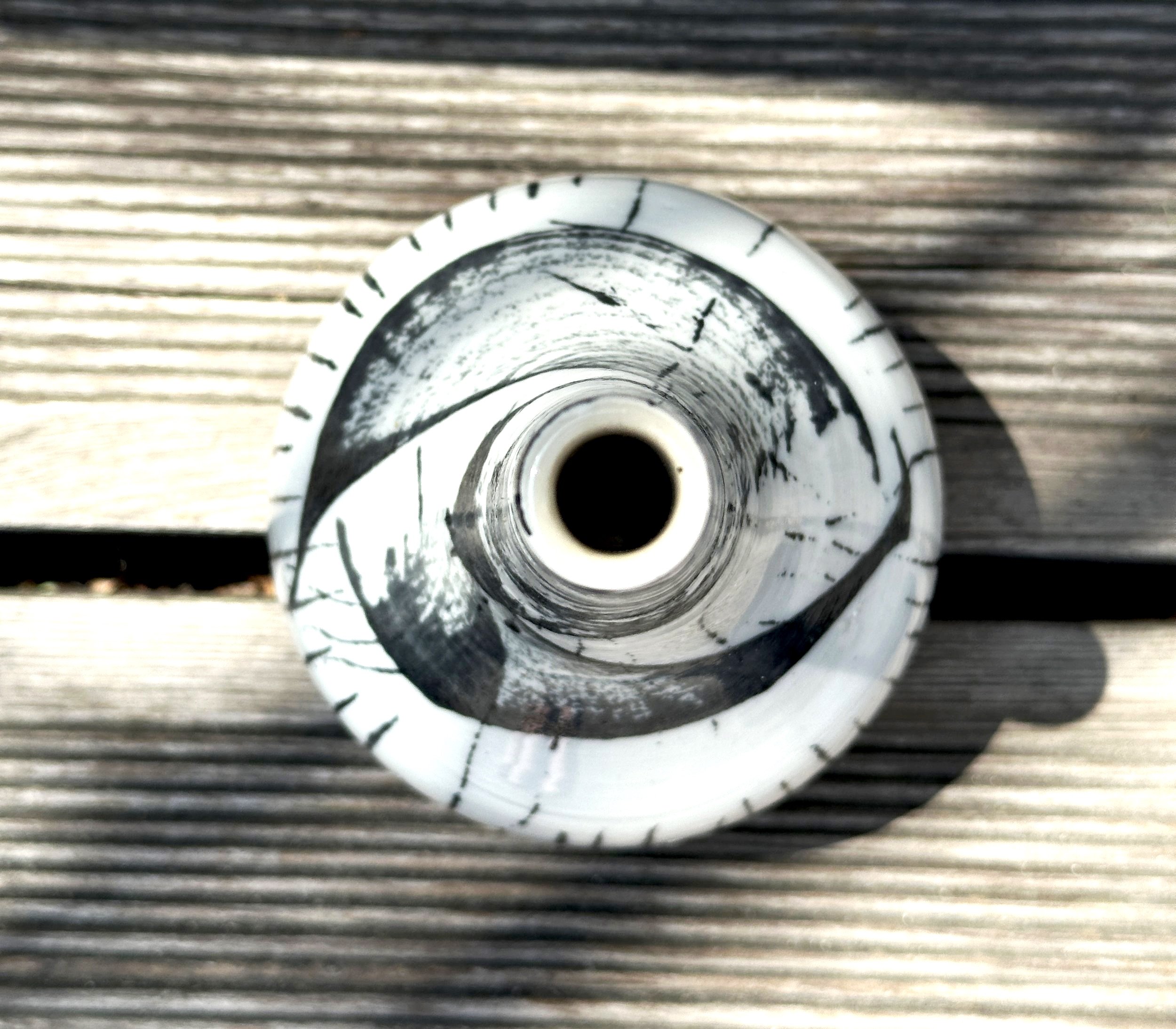 Von oben fotografierte, schmale, lange Flasche auf Holzplanken, schwarz-weiße Muster auf der Flasche