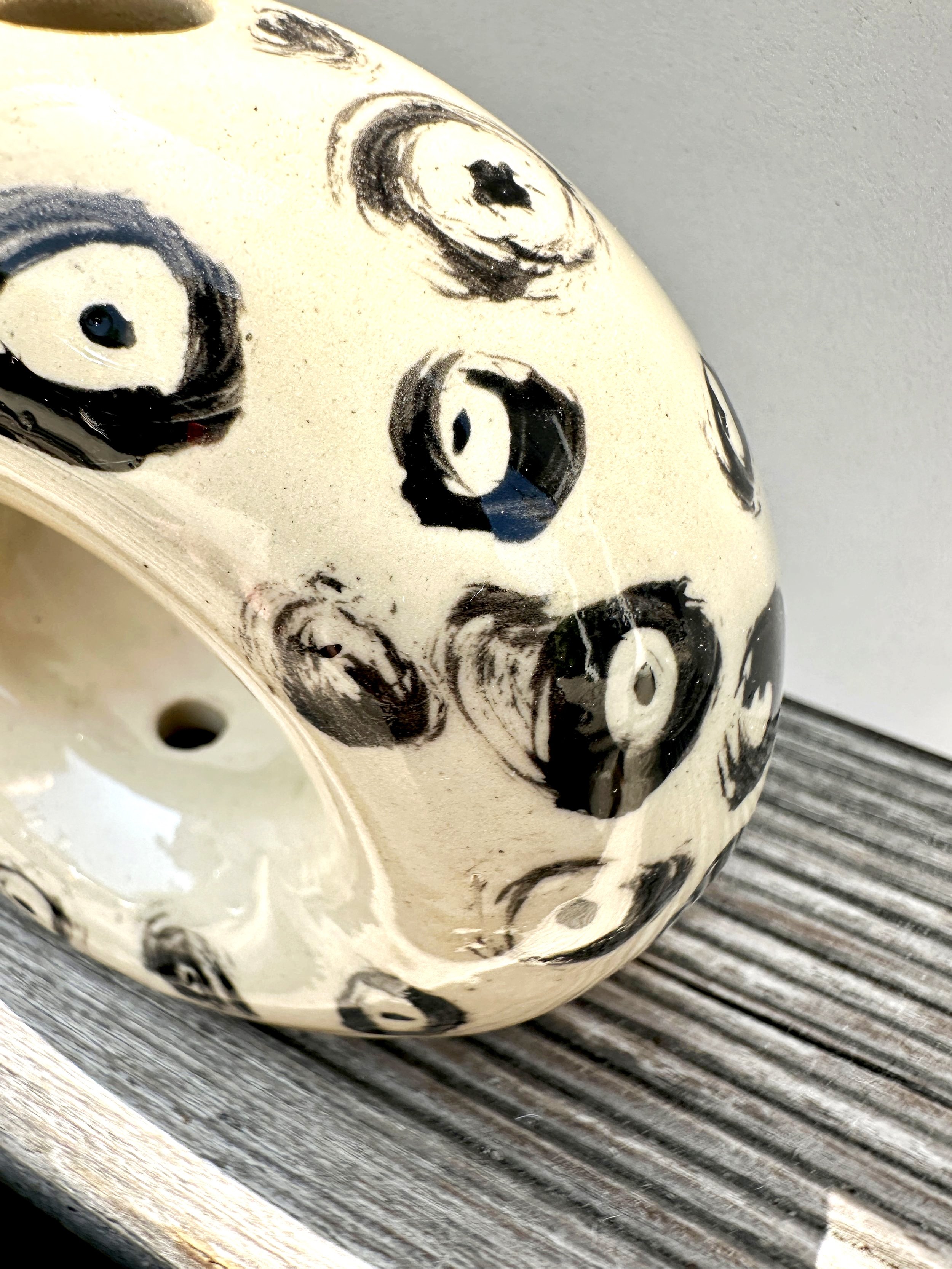 Schwarz-weiße Keramikskulptur mit Augen- und Gesichtsdesign auf einer Holzplattform.
