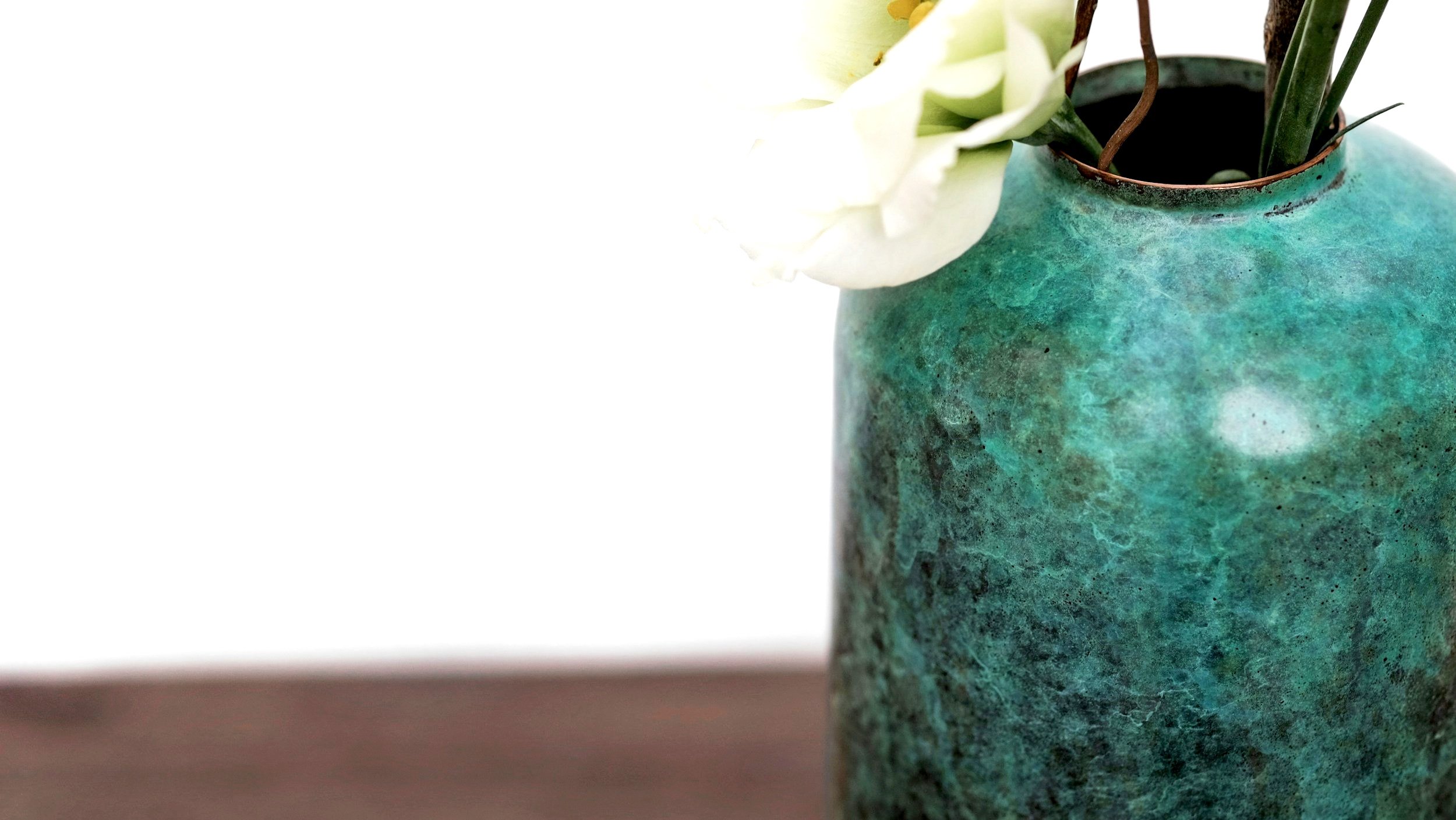 Grüner Keramikvase mit weißen Blumen und grünen Blättern, auf braunem Tisch