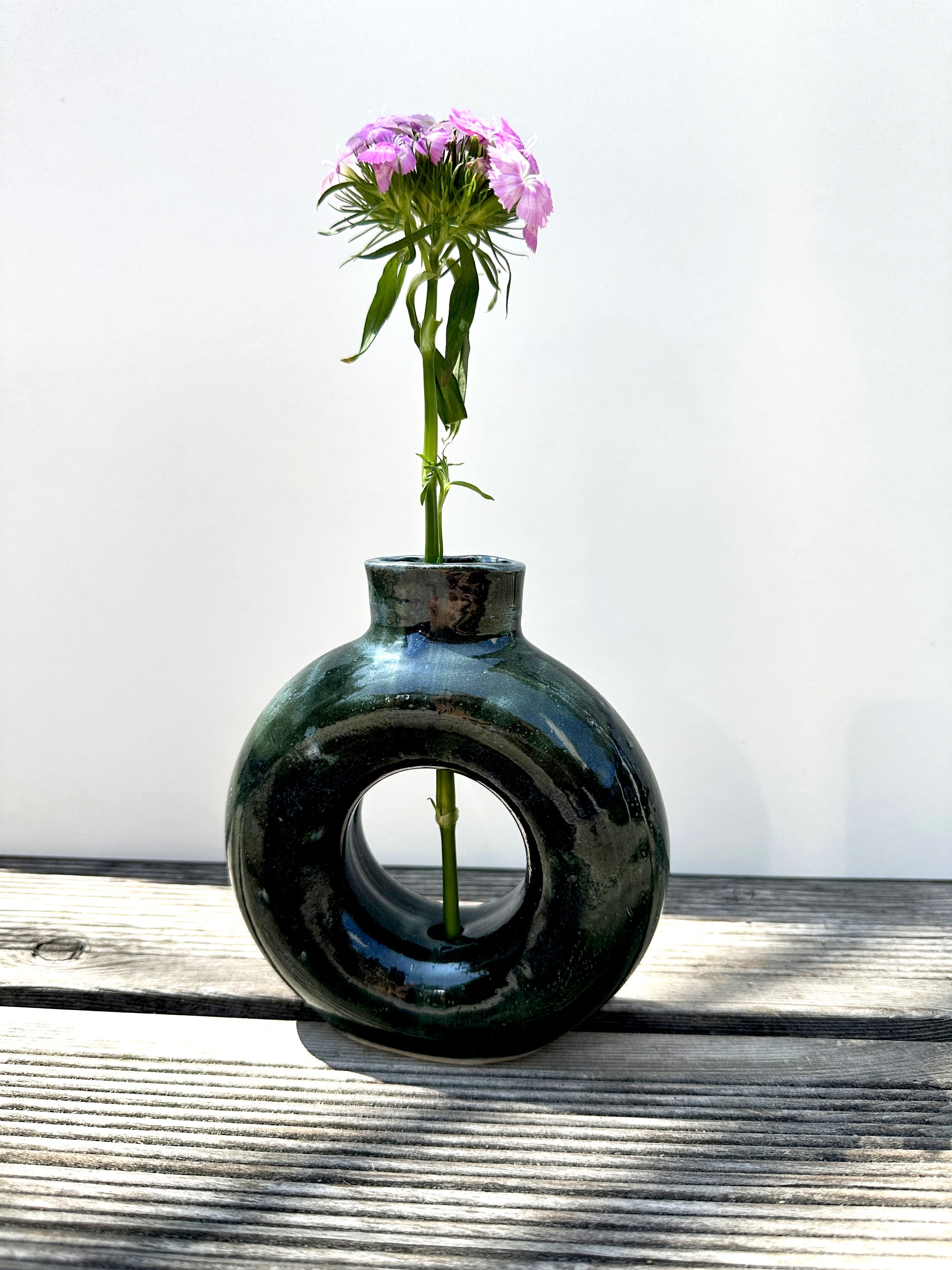 Vase mit einer pinken Blumen auf einer Holzoberfläche vor einem weißen Hintergrund.