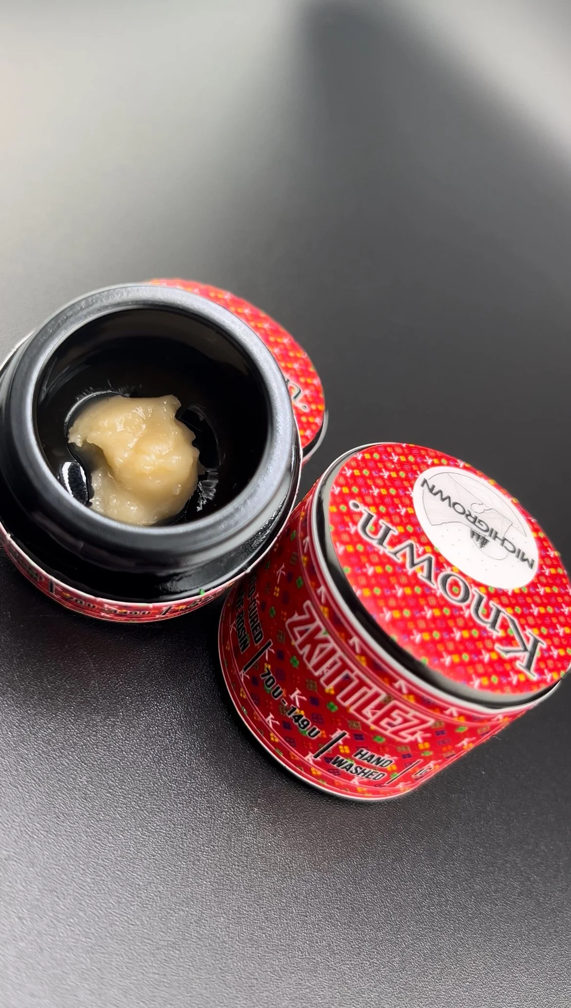 Open jar of strawberry-flavored candy or gummy inside a red container with a spoonful of the candy on a black surface.