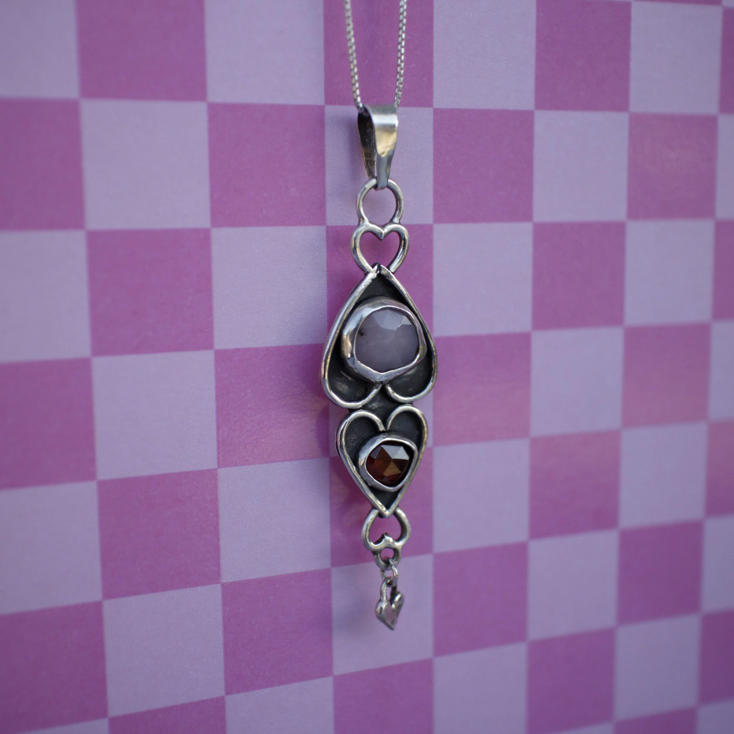 A silver charm with a circular, reflective gemstone in a decorative setting, placed on a navy velvet jewelry box, surrounded by light blue satin fabric.