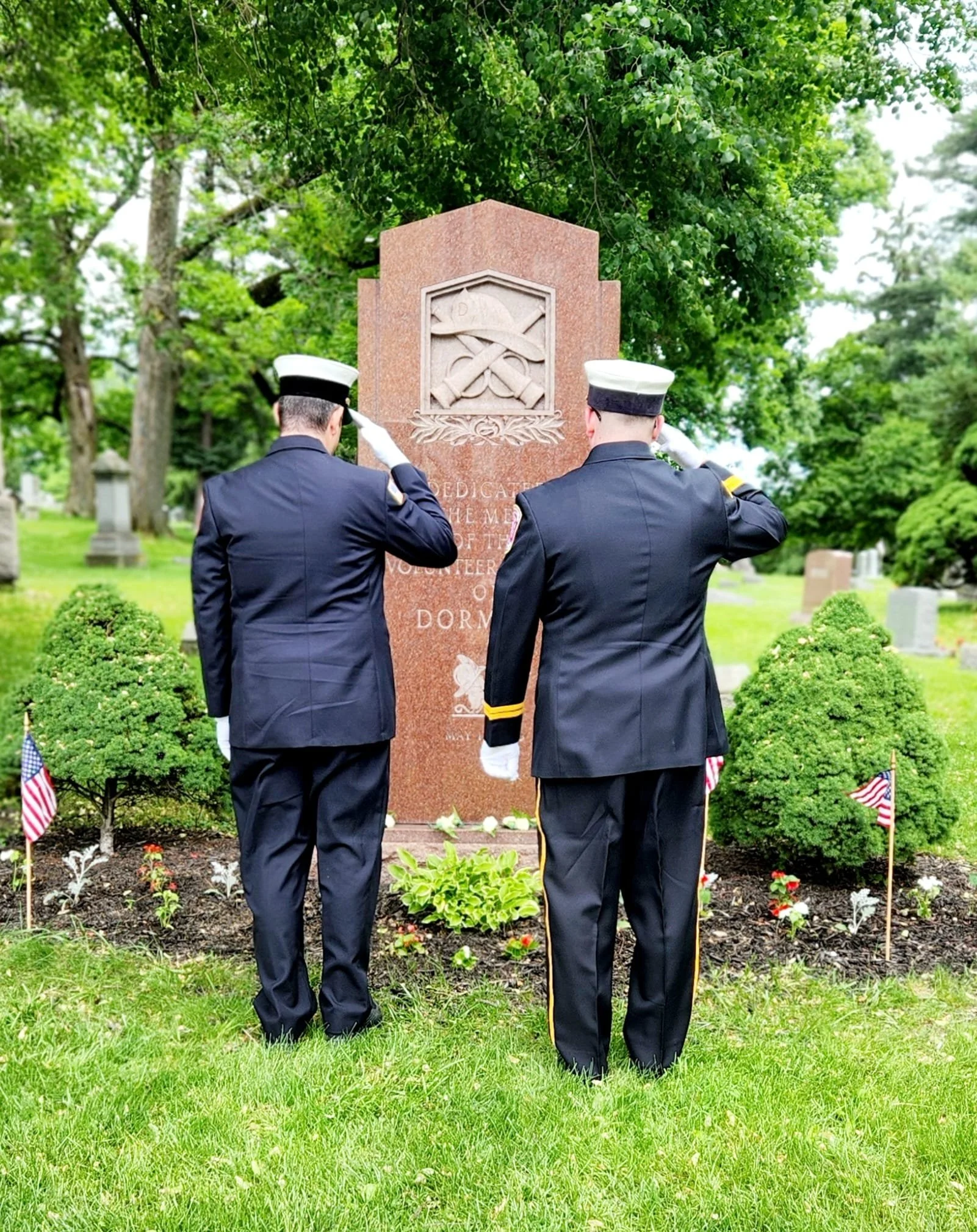 Two uniformed military personnel saluting at a gravesite in a cemetery.