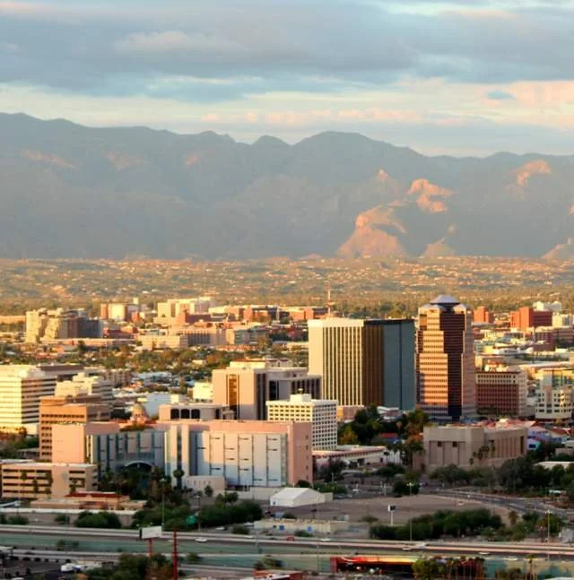 Cityscape with tall buildings and mountains in the background during sunset.