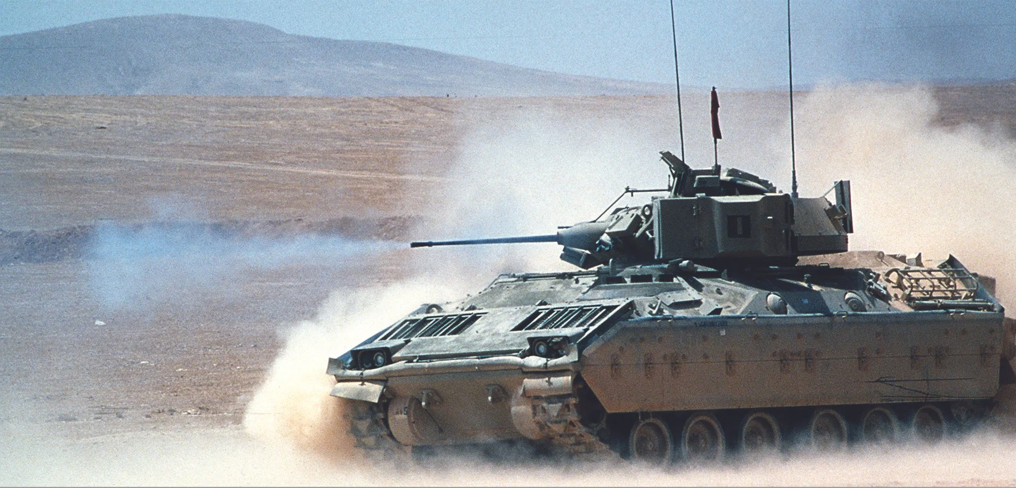 A military tank moving across a desert landscape, kicking up dust.
