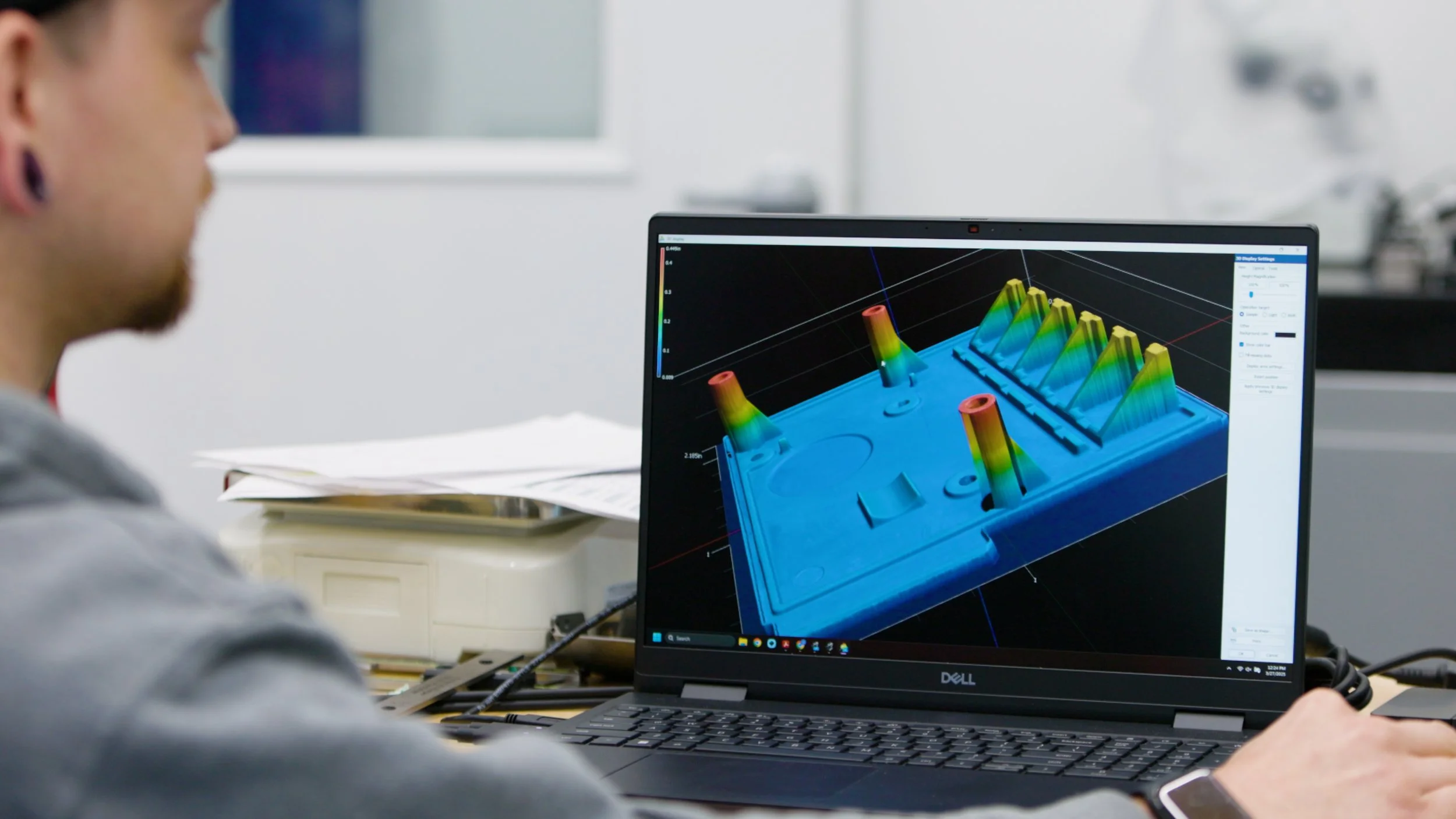 A person working on a computer displaying a 3D graph of a mechanical component with peaks and valleys in different colors.