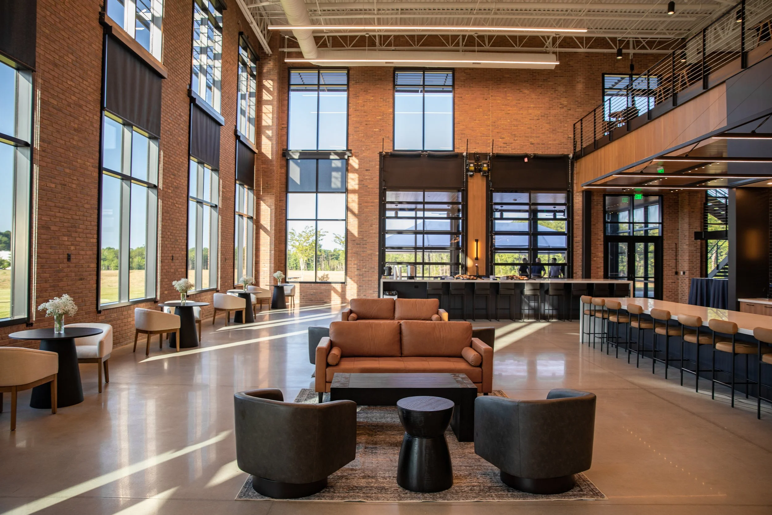 Bright, modern lobby area with large windows, brick walls, and stylish furniture including a sofa and chairs, with a reception or bar area in the background.