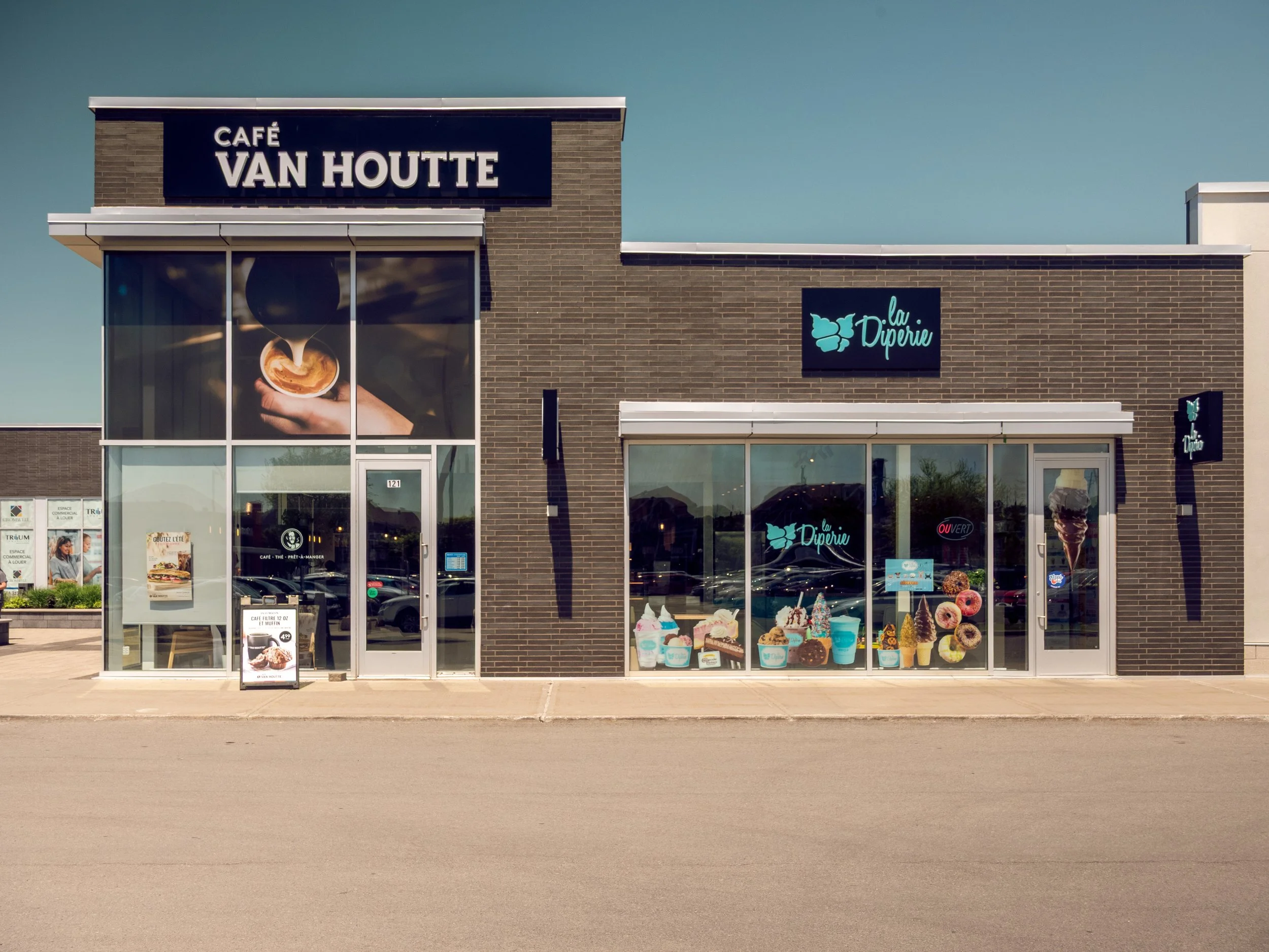 Exterior of a cafe and ice cream shop named Café Van Houtte and La Diperie with large glass windows displaying ice cream and desserts, on a sunny day.