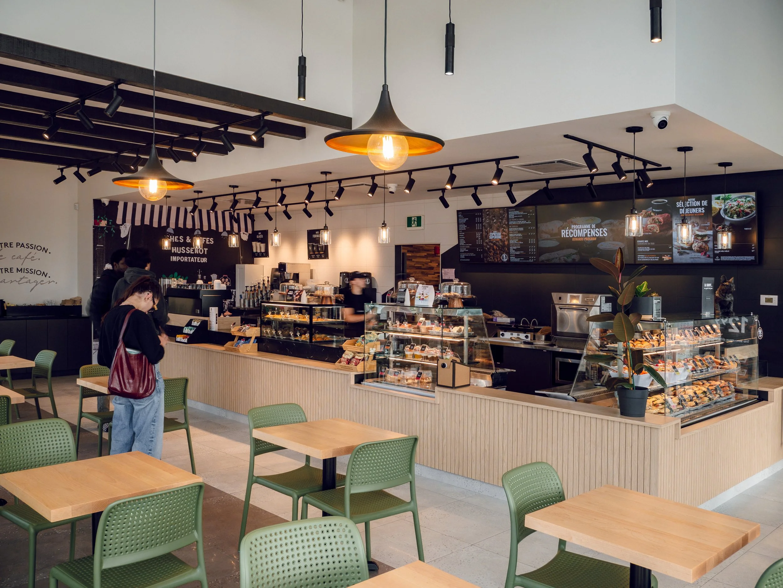 Interior of a modern coffee shop with seating area, display cases of baked goods, and digital menu boards.
