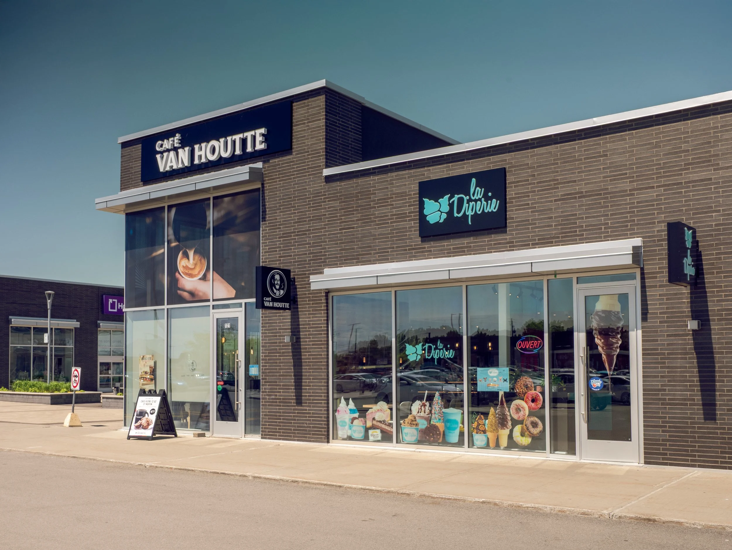 Exterior view of a café named Ladépite with ice cream and dessert displays in the window, and signage for Café Van Houtte, in a shopping plaza.