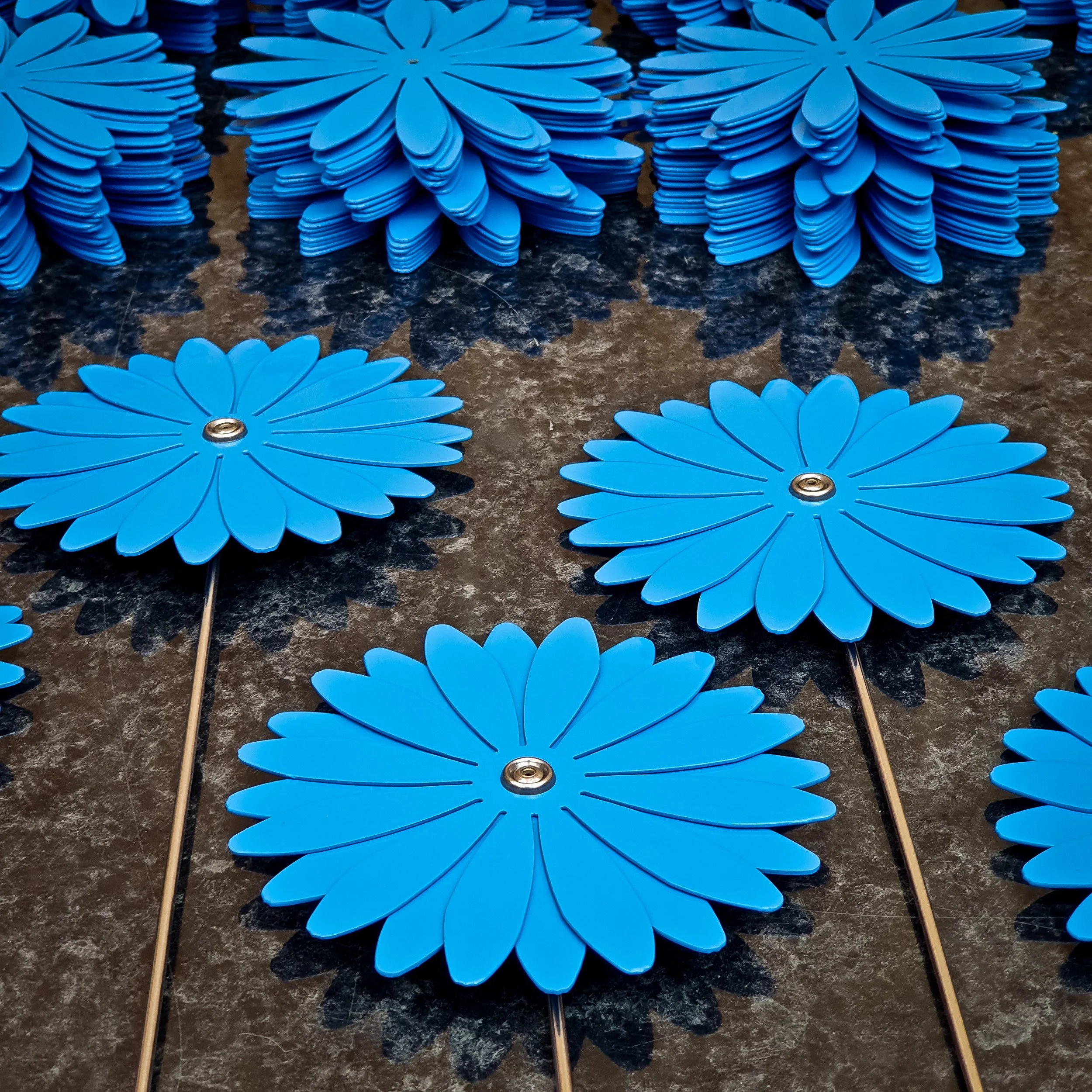 Multiple blue metal daisies stacked ready for assembly.