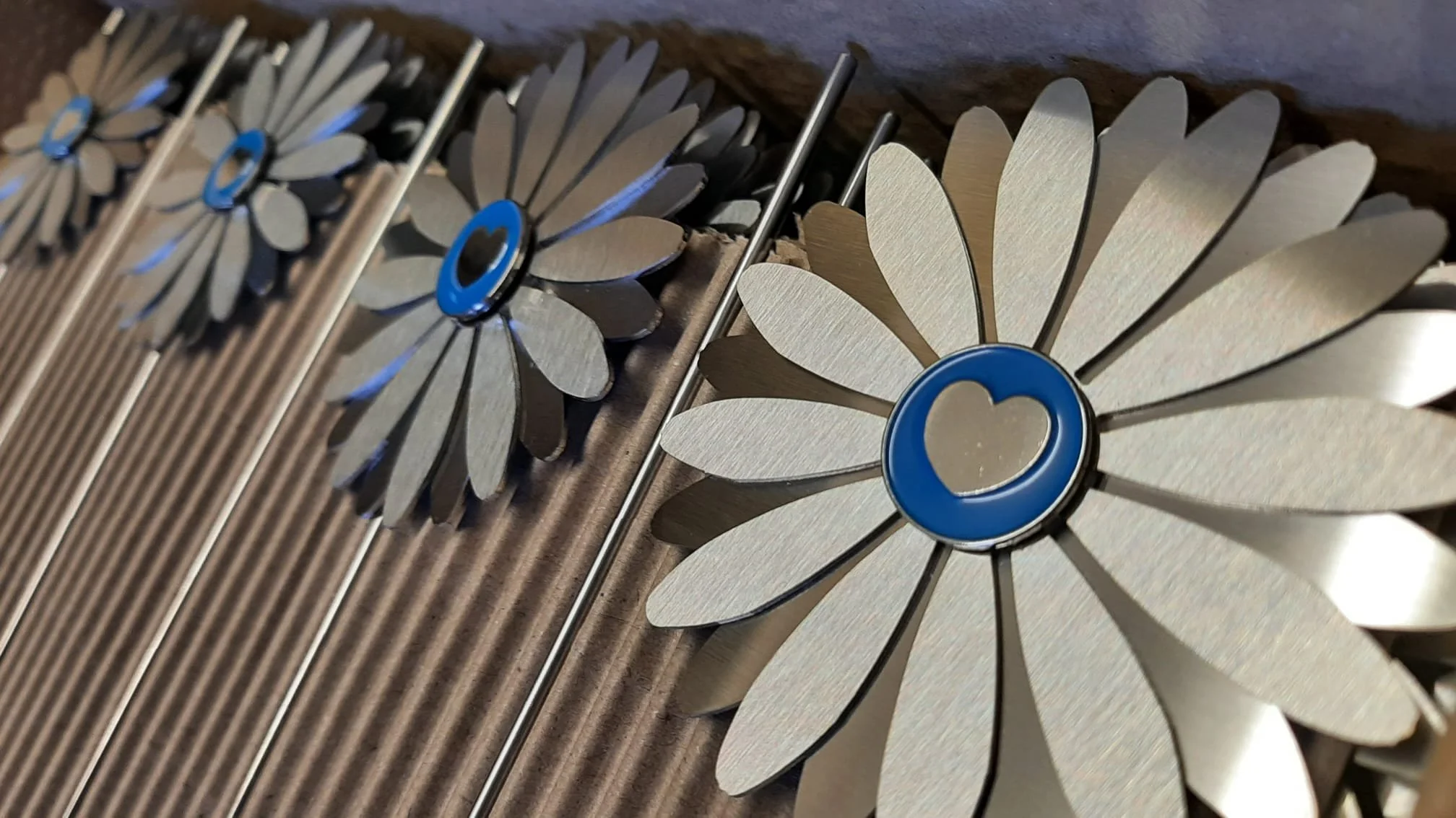 Metal flower-shaped ornaments with blue heart center, arranged in a row on a textured surface.