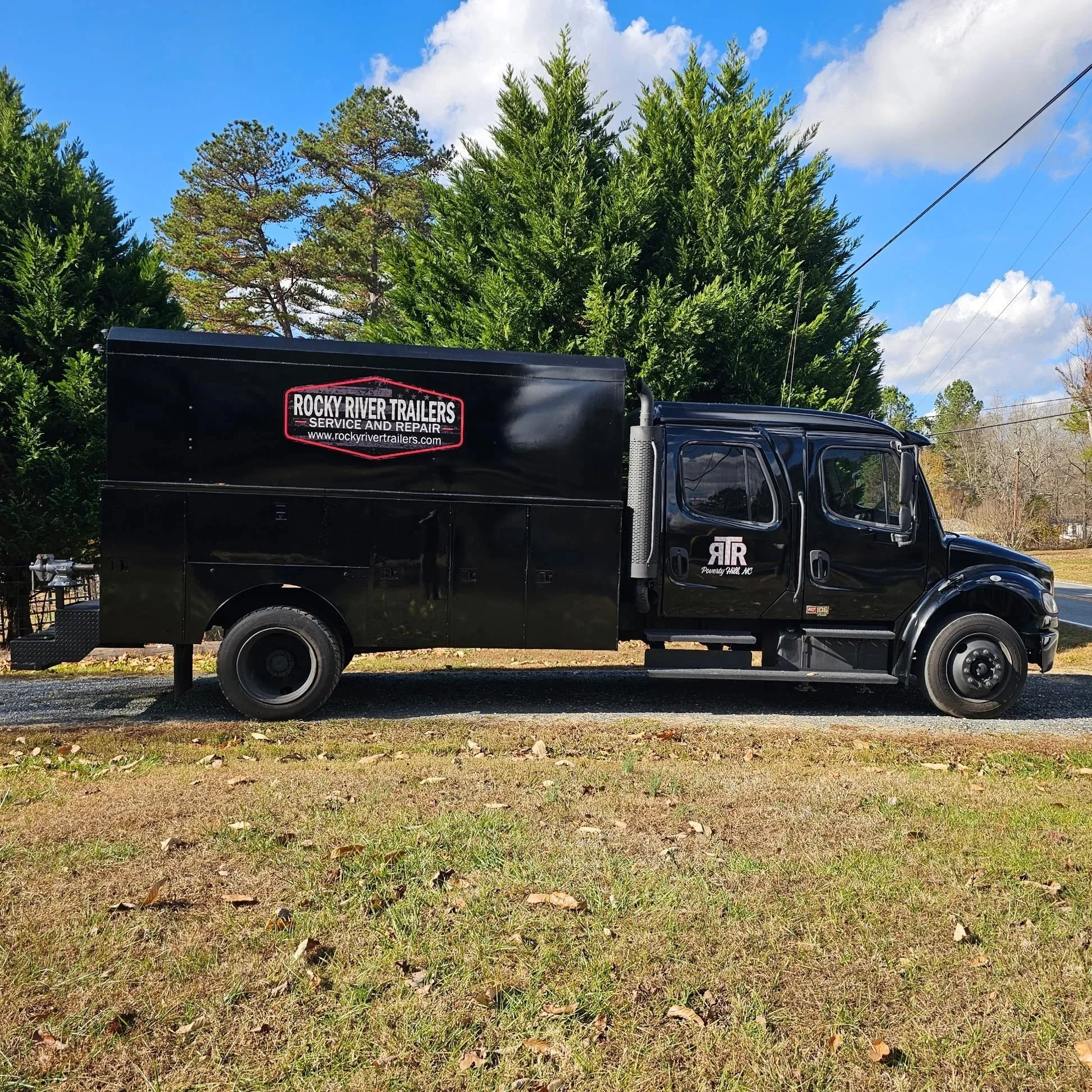 Black service truck parked on a grassy area with trees and a blue sky in the background, advertising Rocky River Trailers for repair services.