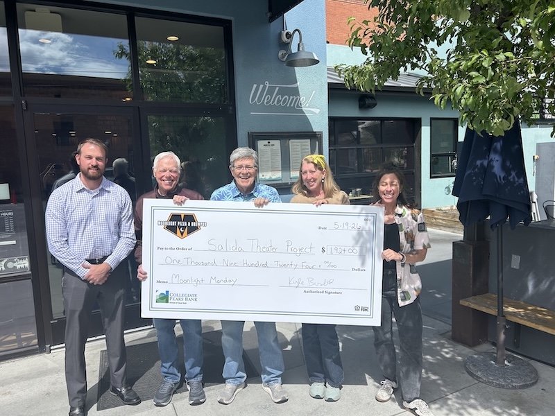 Five people standing outside a building holding a large check for the Salida Theater Project, dated 5-19-26, with a Harley-Davidson logo on it.