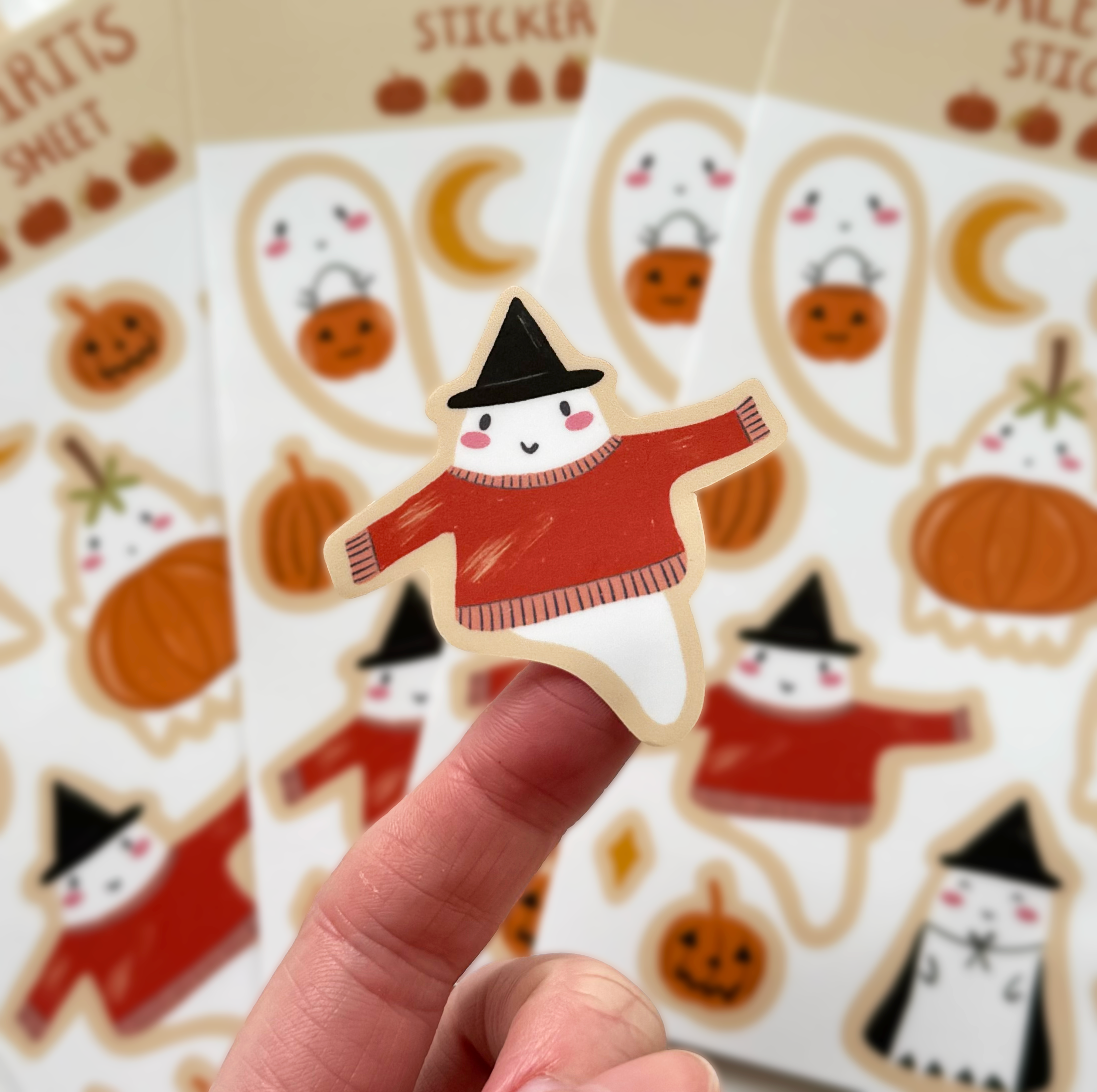 Close up of a ghost sticker wearing a black witch hat and a cozy red sweater.