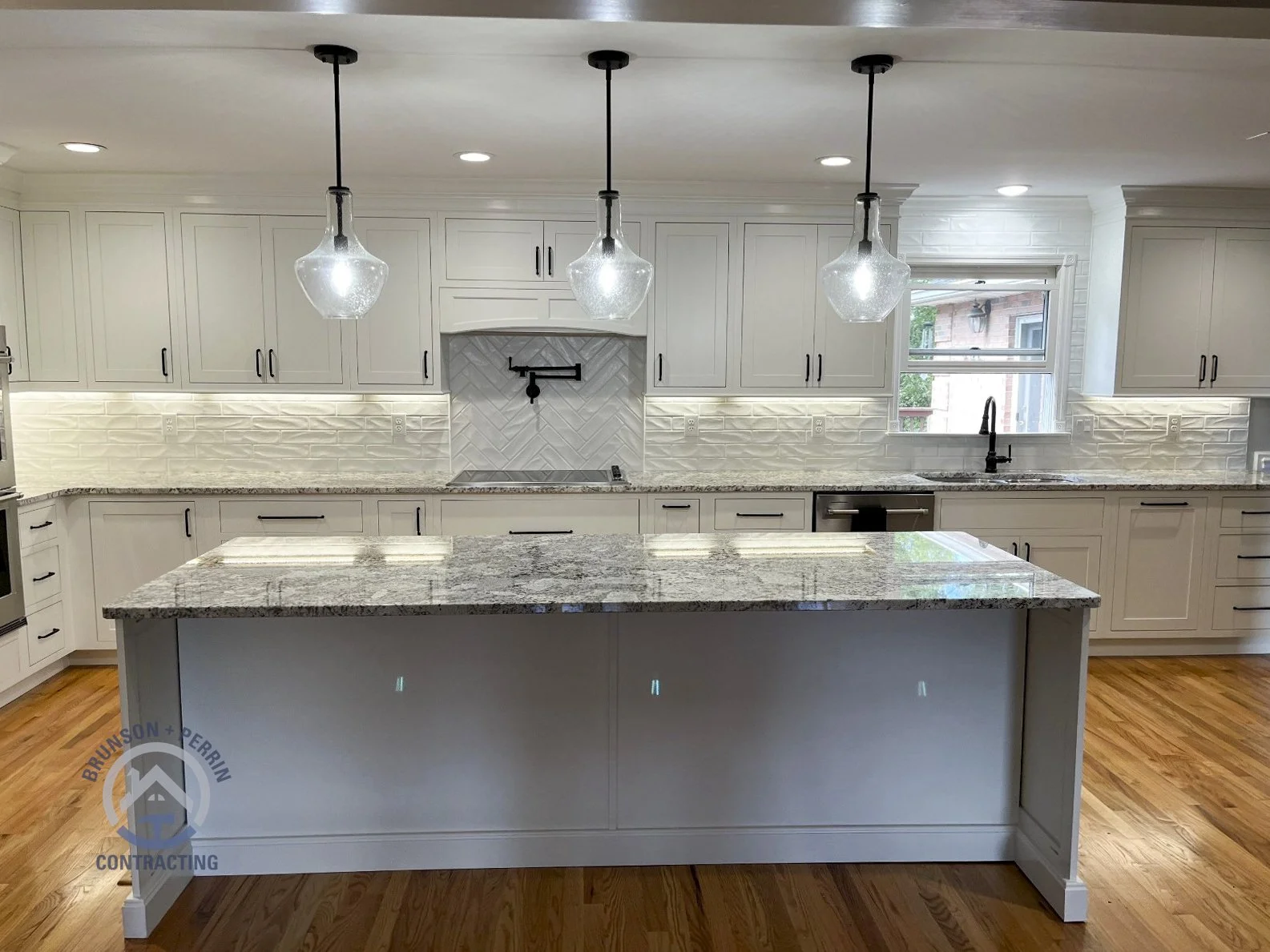 Spacious custom kitchen with white shaker cabinets, matte black hardware, granite countertops, large island, pendant lighting, custom tile backsplash, and matte black pot filler – Johnson City, TN remodel. Partnership with Katy Lynn Cabinetry & Desig