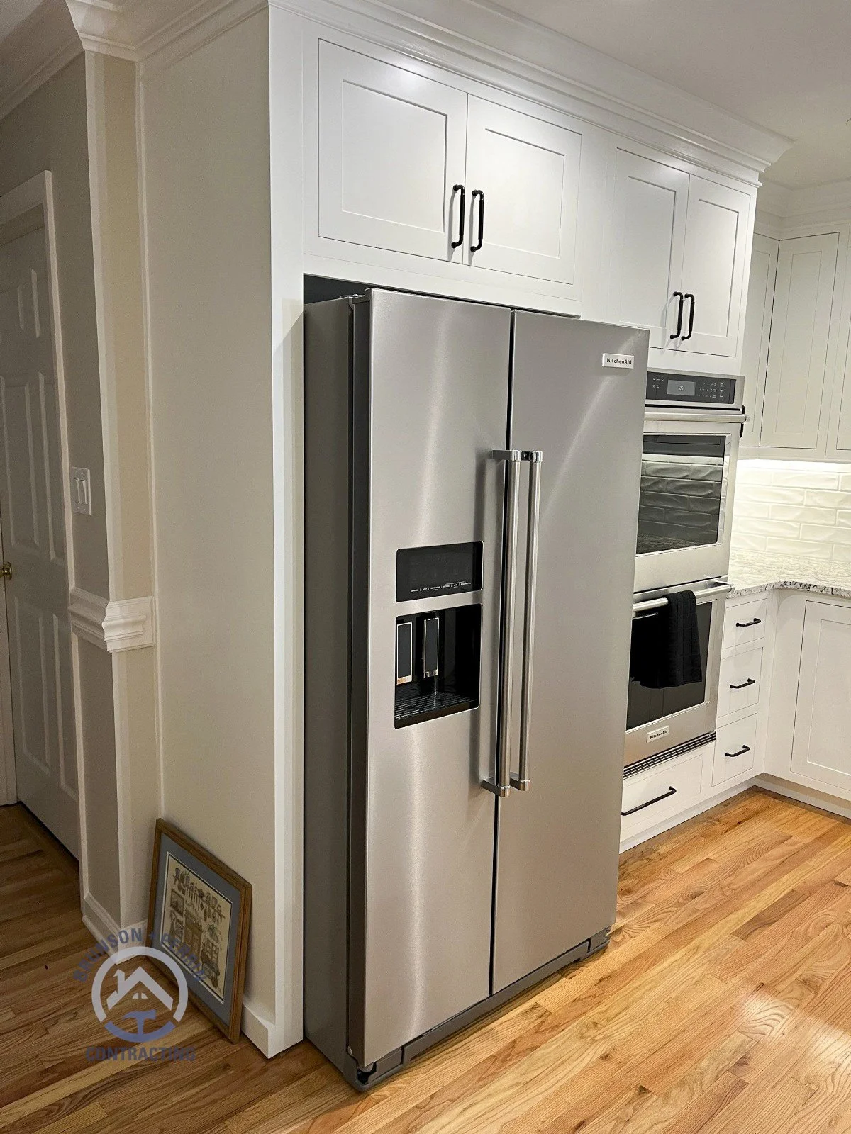 White shaker cabinets with matte black hardware, granite countertops, textured white tile backsplash, stainless steel appliances, and natural wood flooring – custom kitchen remodel in Johnson City, TN. Partnership with Katy Lynn Cabinetry & Design