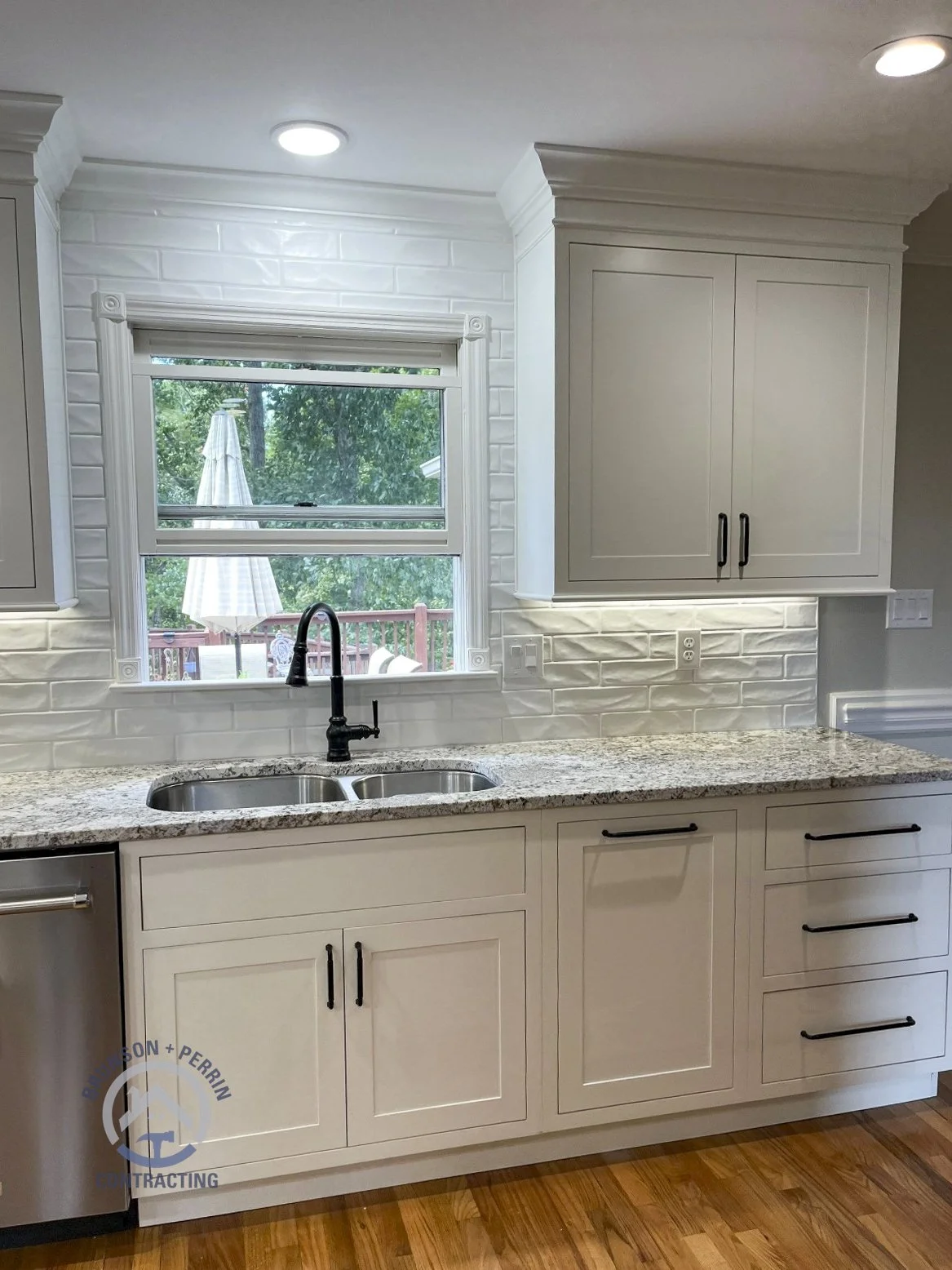 White shaker cabinets with matte black hardware, granite countertops, a double-basin sink, matte black faucet, and a white textured tile backsplash in a custom Johnson City, TN kitchen remodel. Partnership with Katy Lynn Cabinetry & Design.