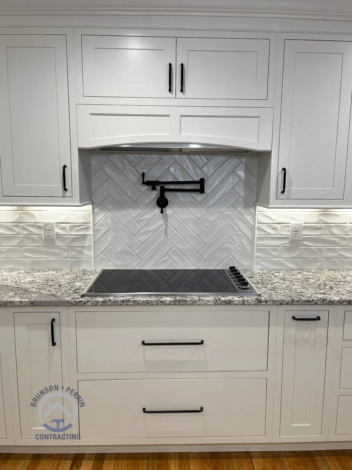 Custom kitchen cooktop area with white shaker cabinets, matte black hardware, granite countertops, herringbone tile backsplash, and a matte black pot filler – Johnson City, TN remodel. Partnership with Katy Lynn Cabinetry & Design