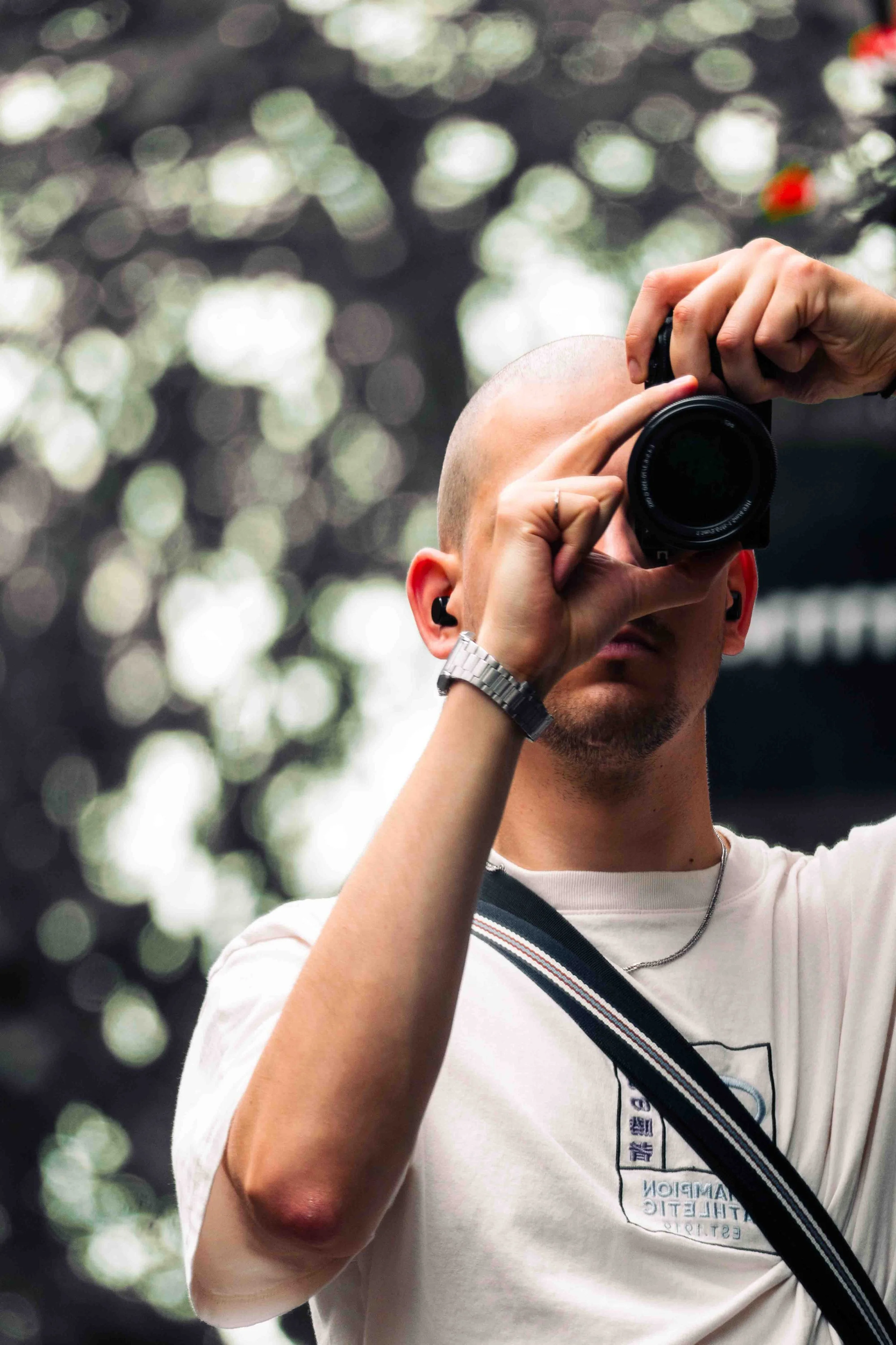 Man neemt een foto met een digitale camera, omringd door een bokeh-effect van licht en bladeren in de achtergrond.