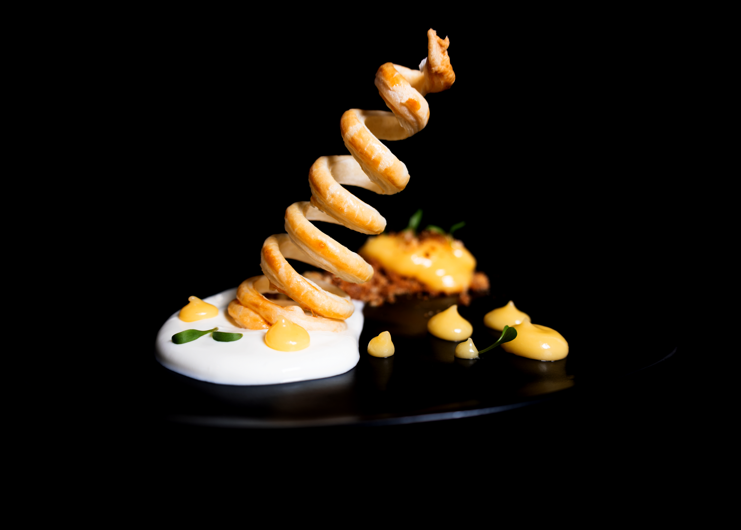Assiette gastronomique élégante avec spirale croustillante dorée sur crème blanche et graines torréfiées, photographie culinaire professionnelle
