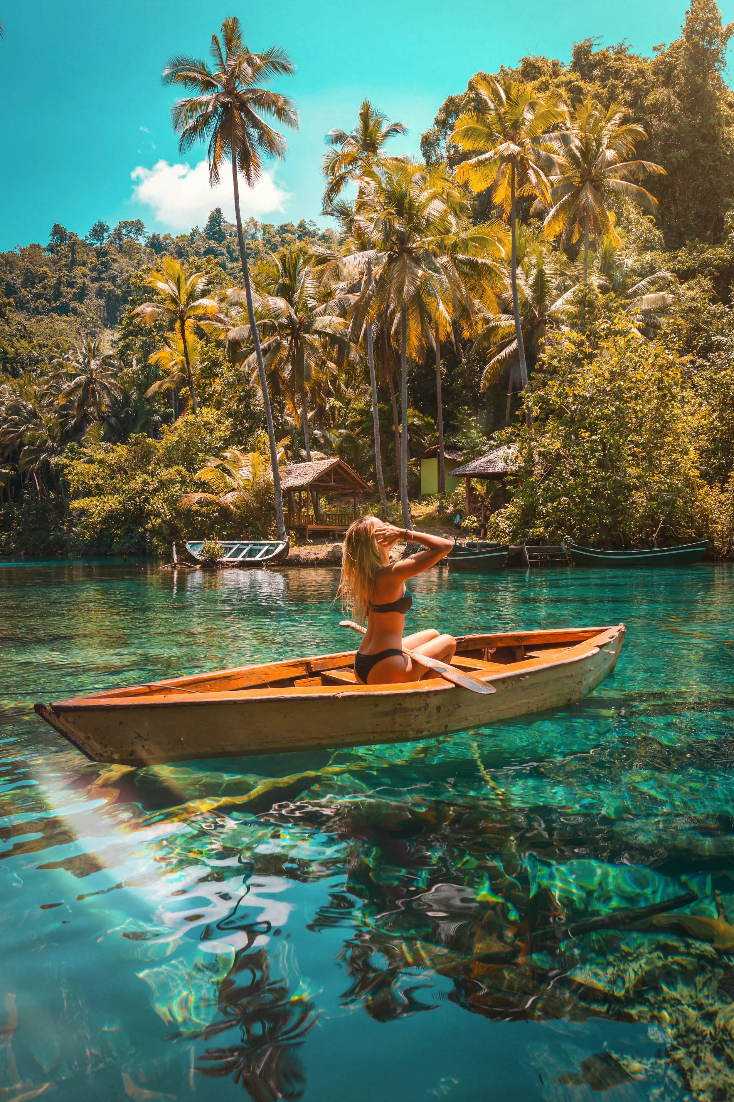 Femme assise dans une barque en bois sur un lagon turquoise transparent entouré de palmiers et végétation tropicale