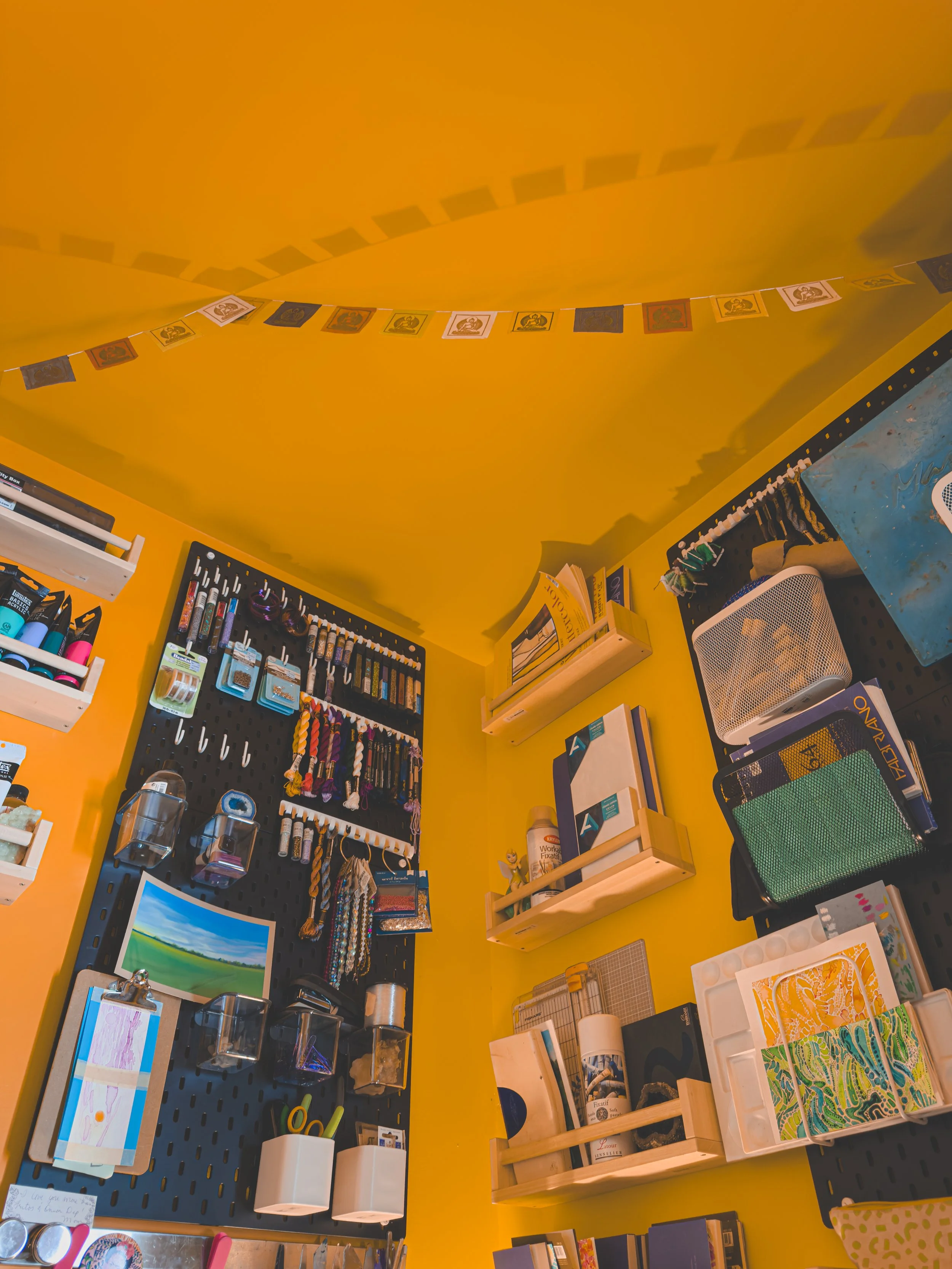 Interior of a craft or stationery store with yellow walls, displaying various art supplies, notebooks, and decorative items on shelves and pegboards.