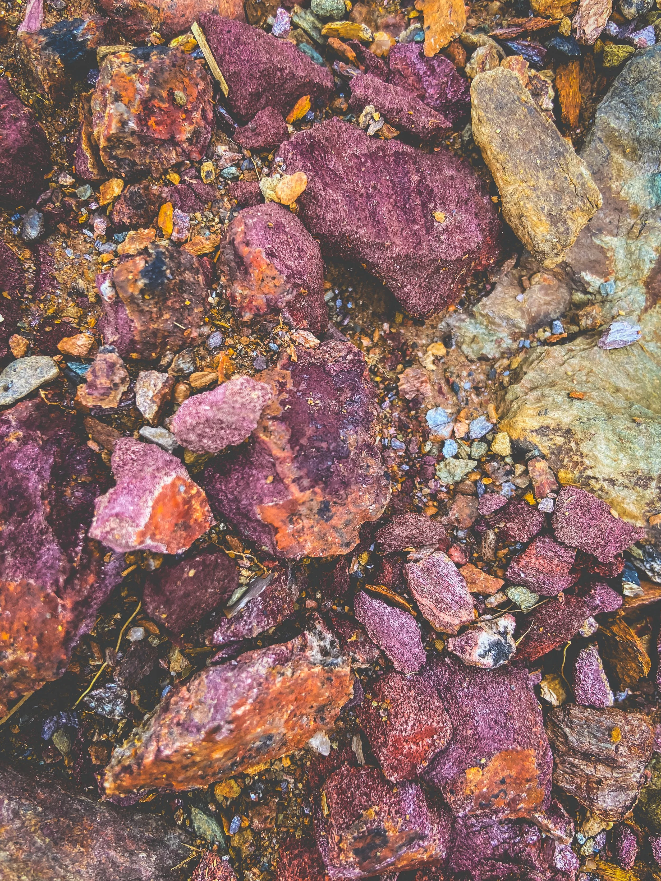 Close-up of various rocks and gravel in earthy tones, including purple, orange, yellow, and gray.
