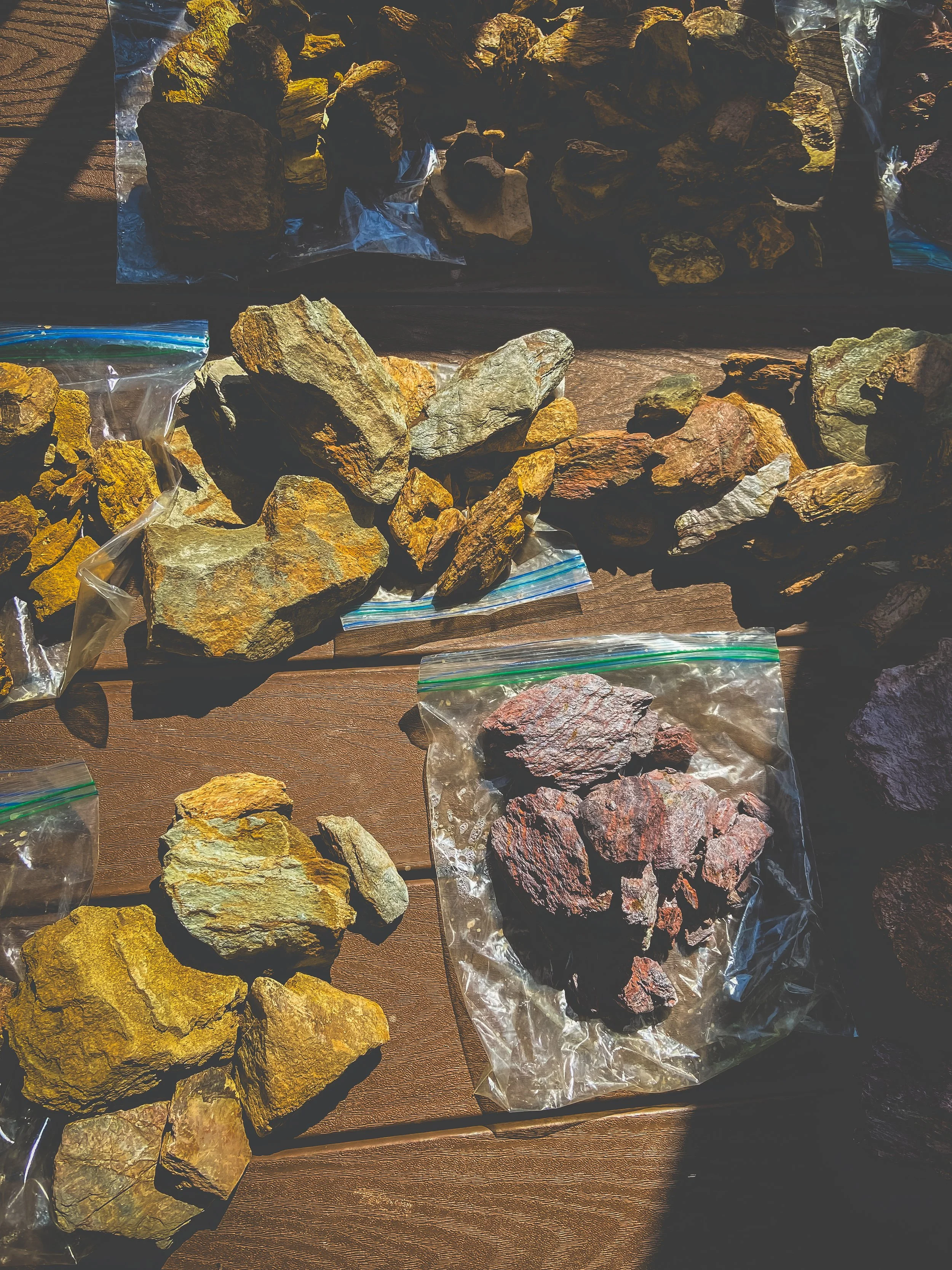 Various types of rocks and minerals in plastic bags and on a wooden surface.