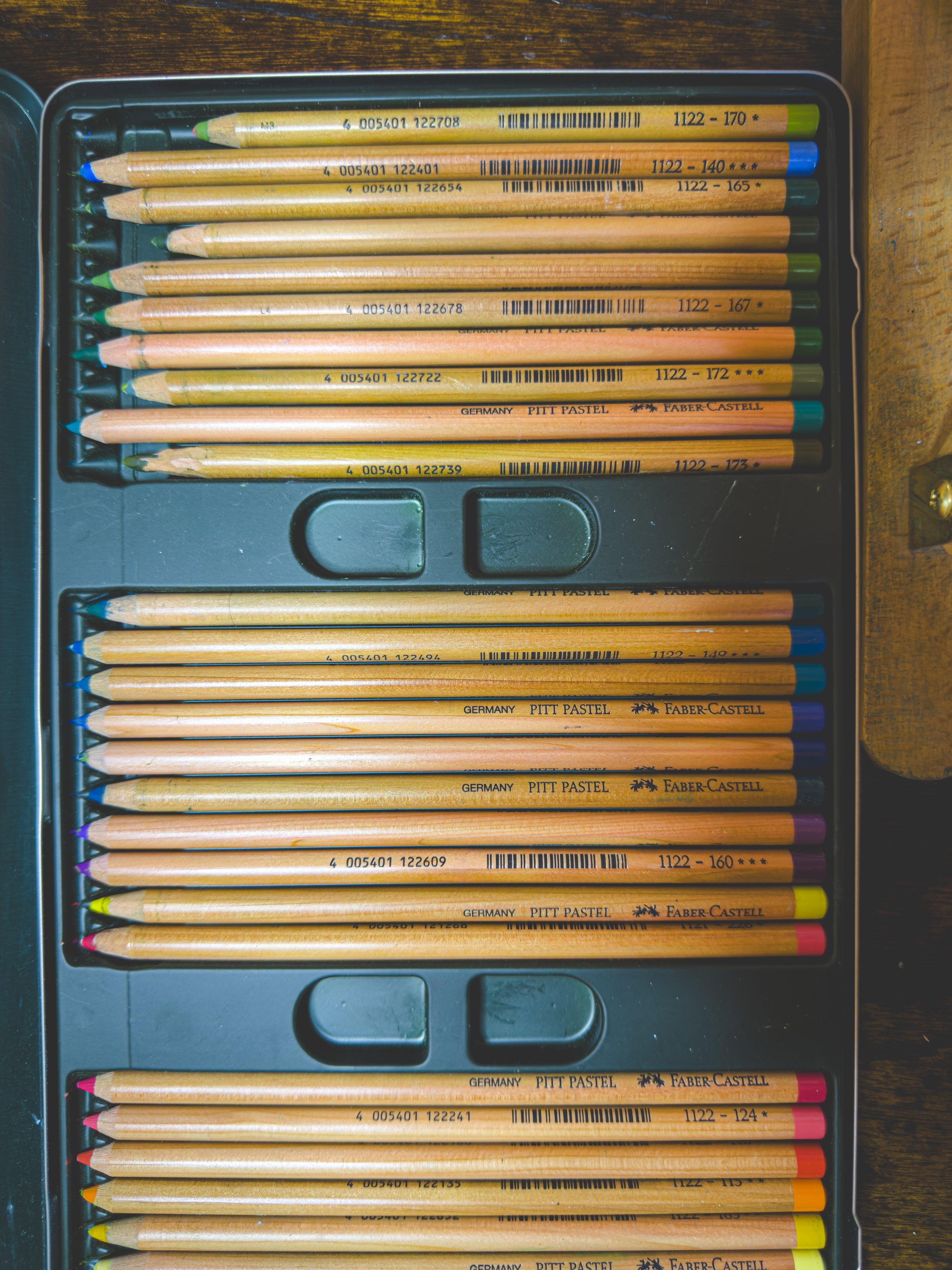 Box of colored Faber Castell PITT Pastel pencils arranged horizontally with various colors and labels.