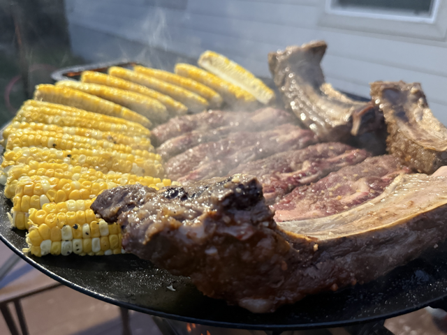 Corn on the cob and steaks grilling on a barbecue grill outdoor.