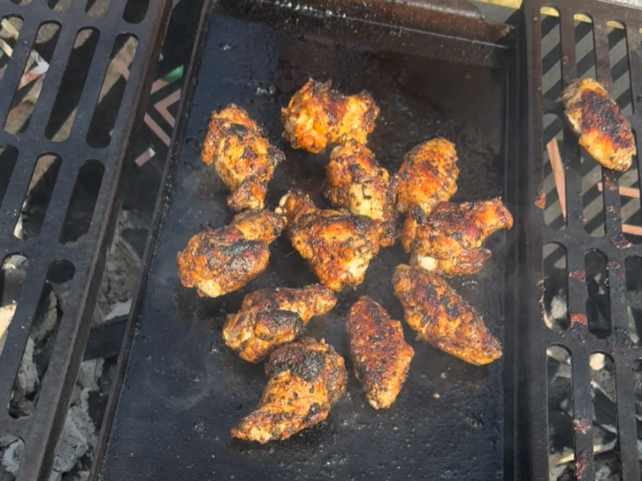 Cooked chicken wings on a grill, some with a smoky, charred appearance, on a black grilling surface.