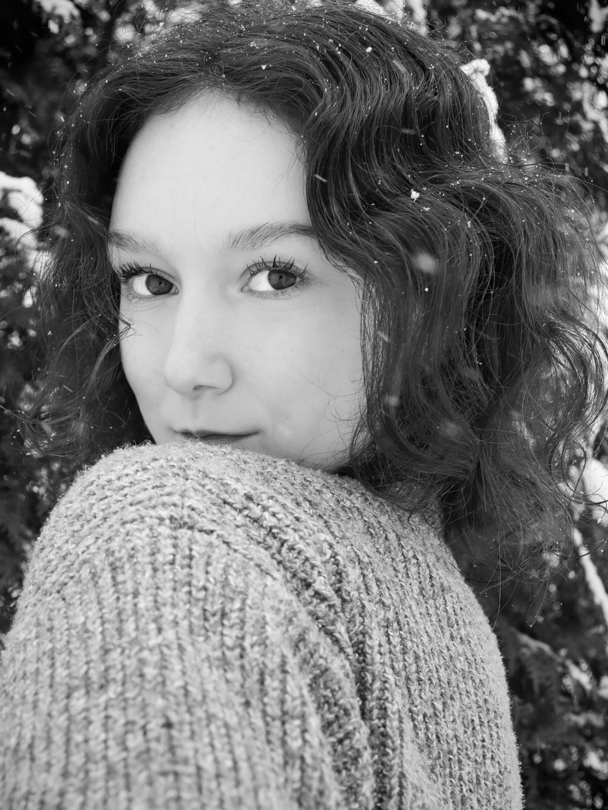 A young girl with curly hair looks over her shoulder at the camera in a snowy outdoor setting.