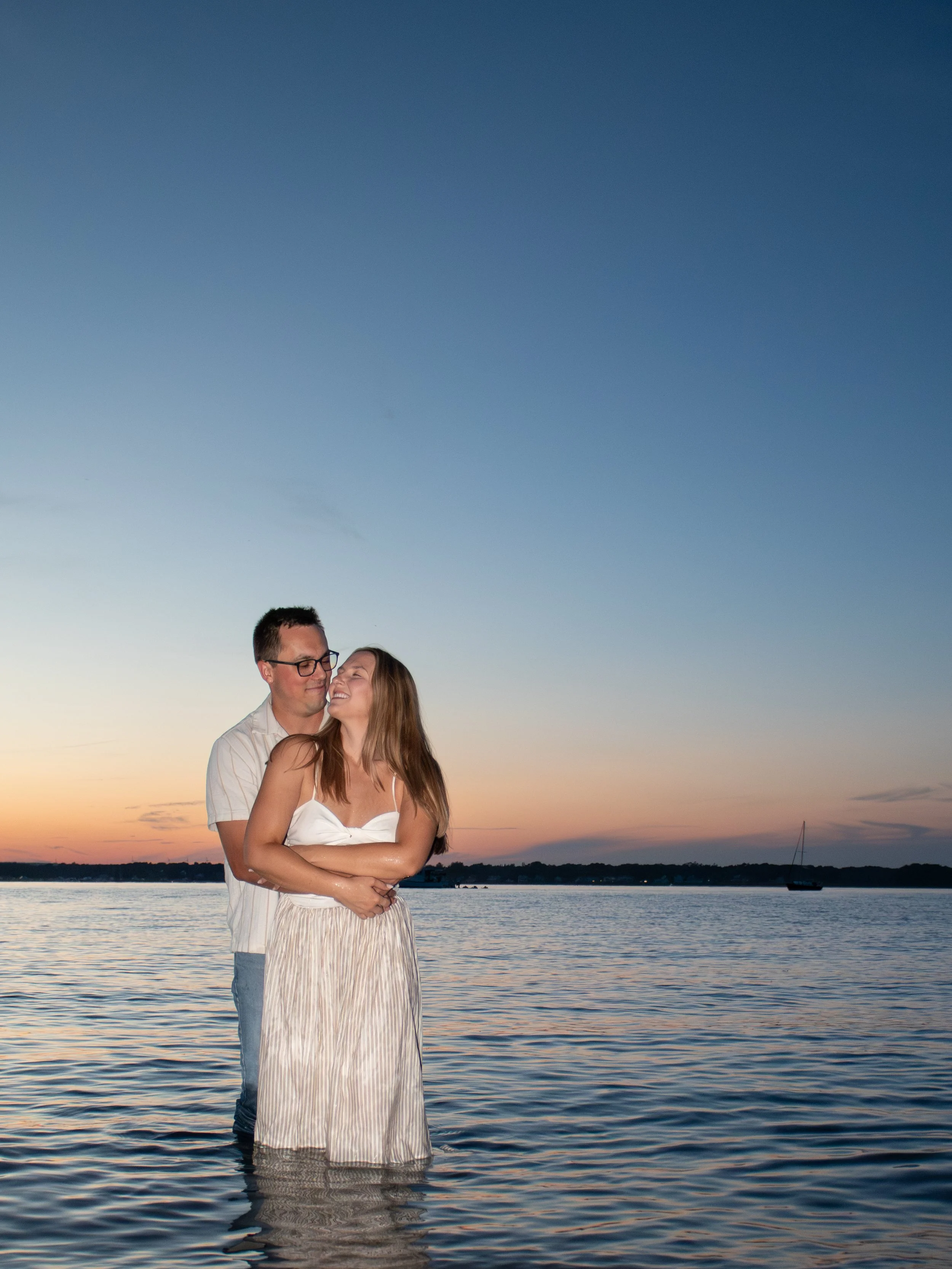 A couple standing in the water near a beach at sunset in Warwick Rhode Island.