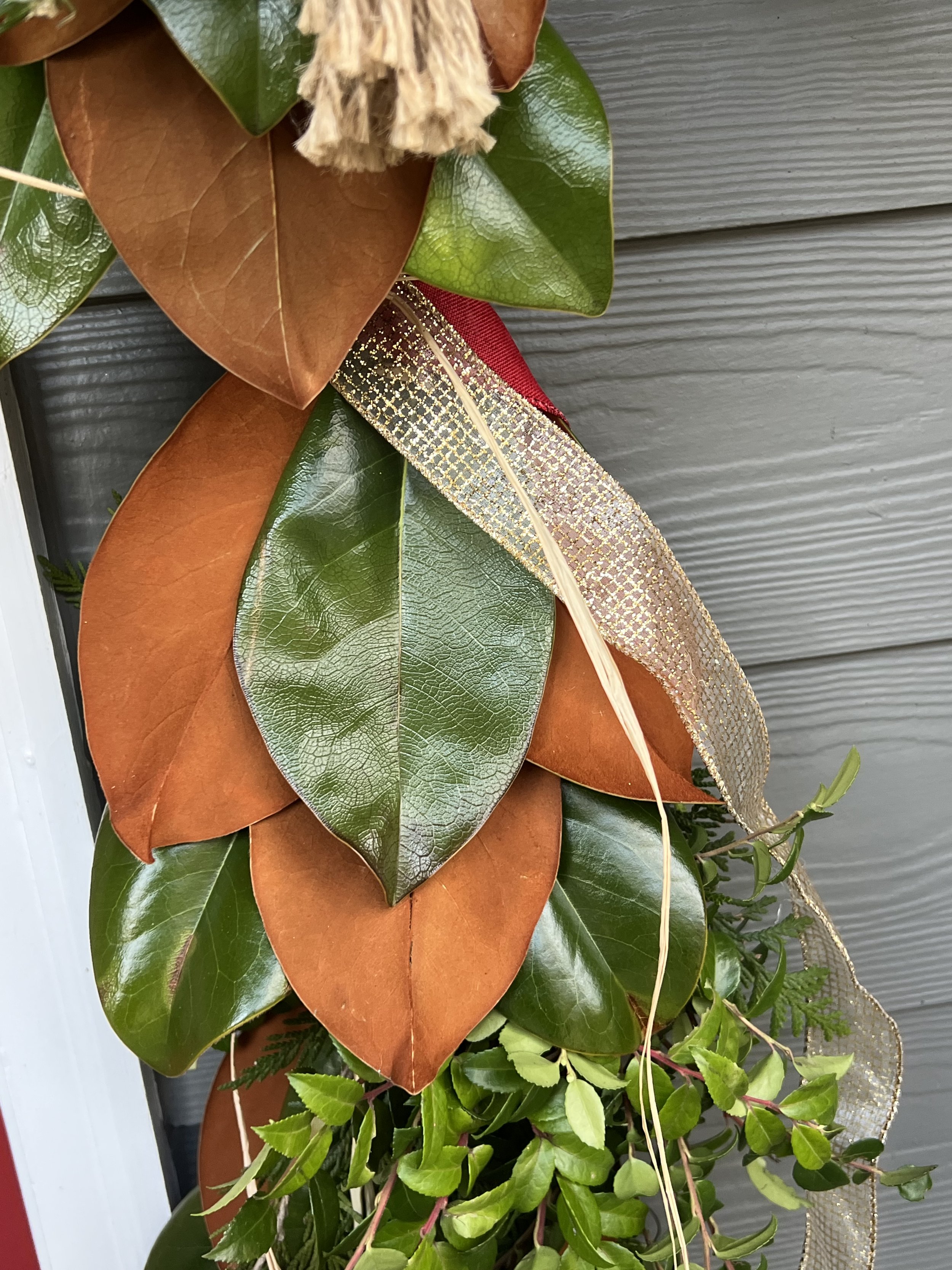Close-up of a Christmas Front Door Decoration with Magnolia leaves, wrapped with a gold and red ribbon, against a gray wooden background in Arnold, MD. 