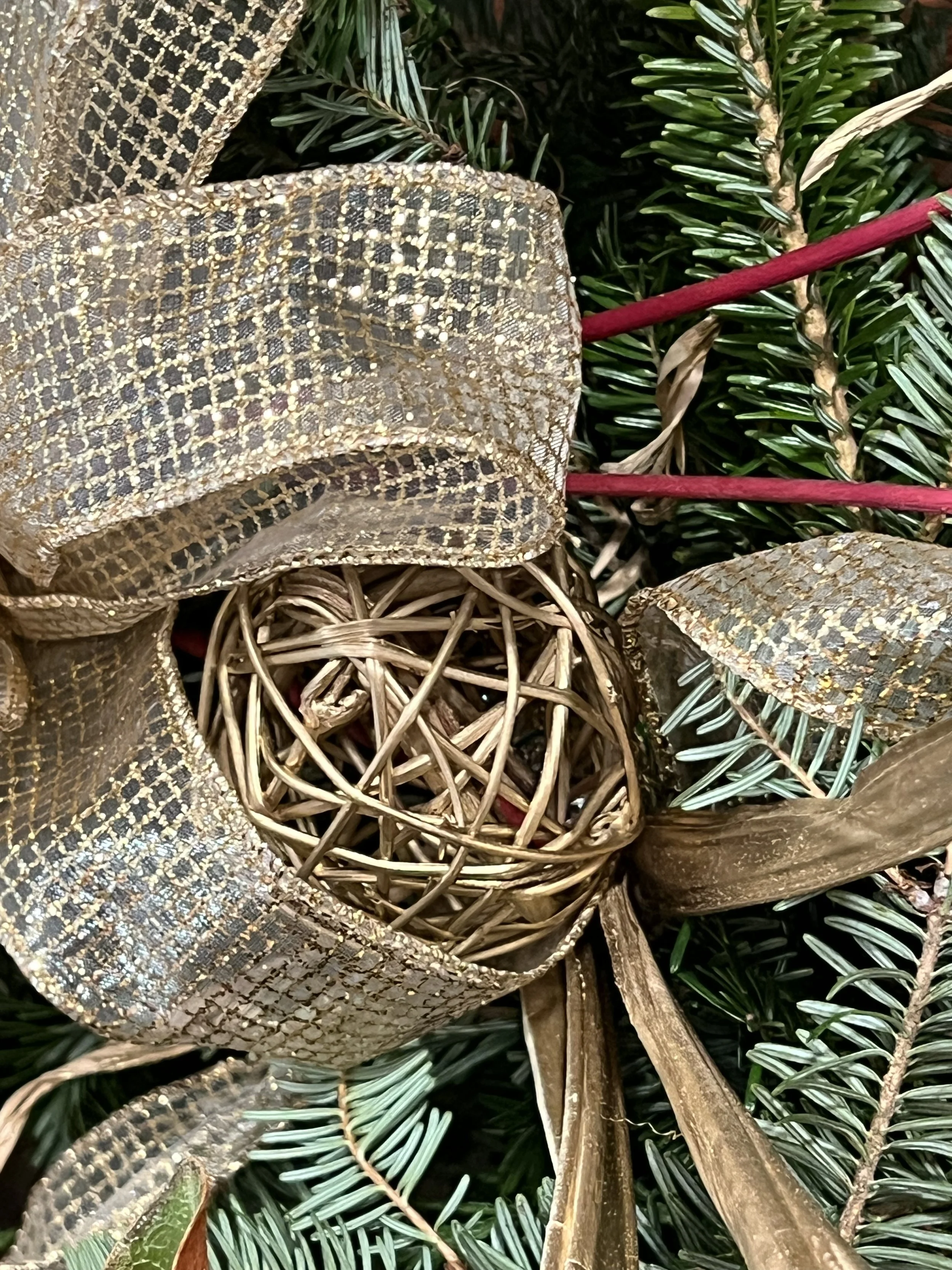 Close-up of a Christmas wreath decorated with gold mesh ribbons, a woven gold ball ornament, and green pine branches in Annapolis, MD.