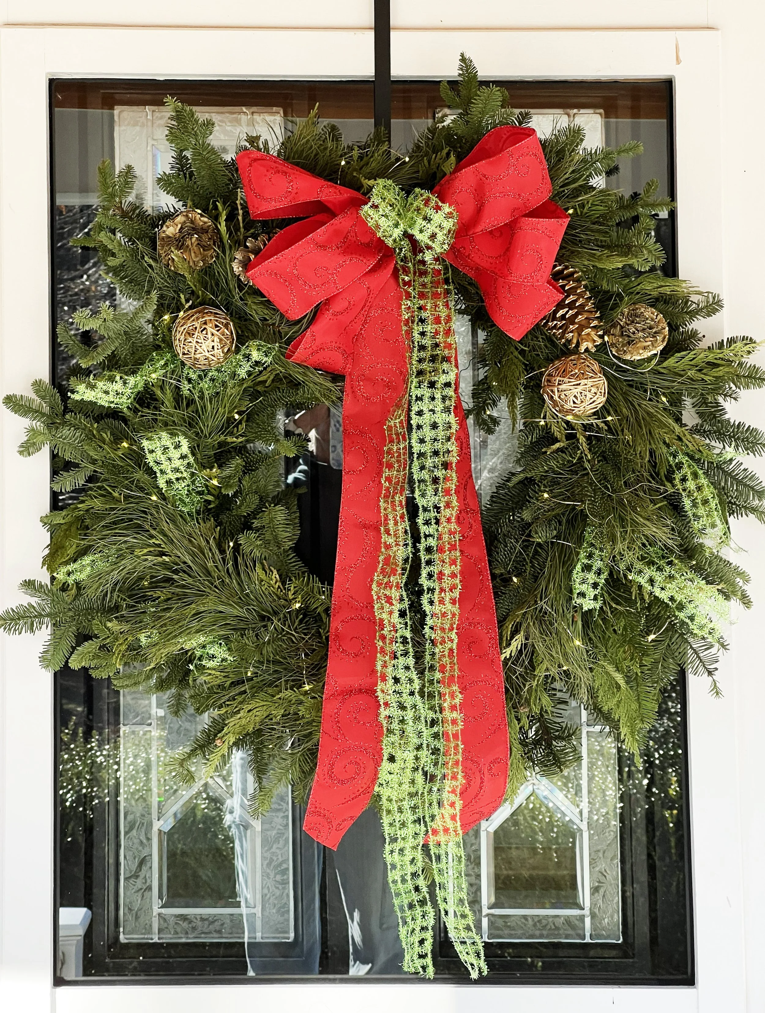 A Christmas wreath decorated with pine branches, gold pinecones, and gold ornaments, adorned with a large red bow and green ribbons, hanging on a door in Arnold, MD.