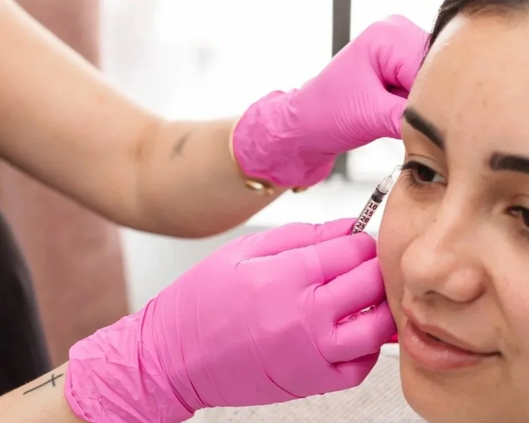A woman getting a cosmetic facial injection while wearing pink gloves.