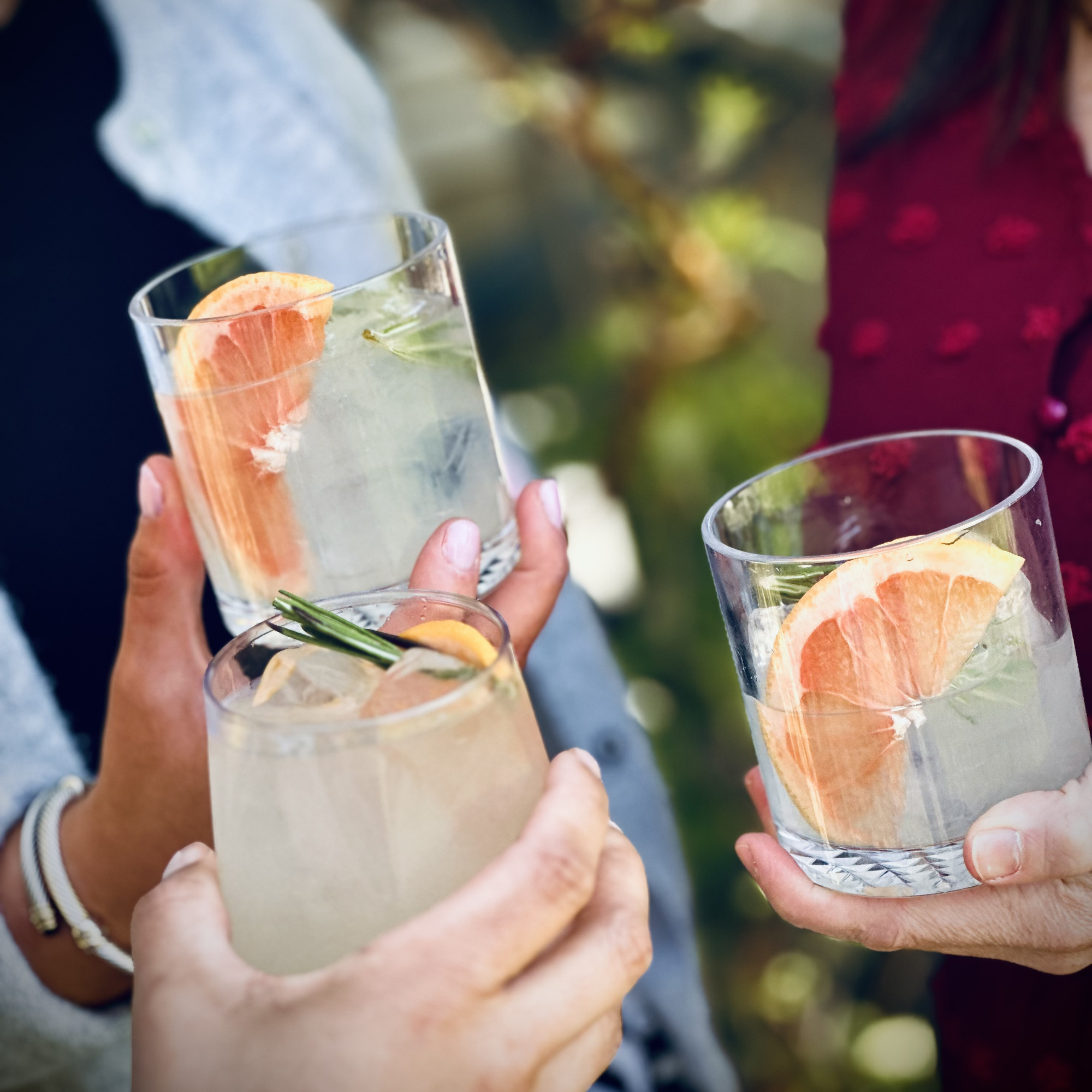 Group of people raising glasses filled with cocktails in celebration outdoors.