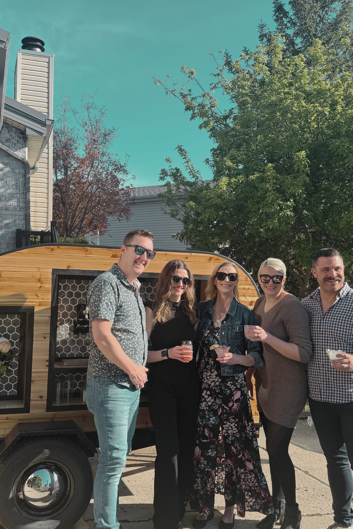 Group of five people standing outdoors in front of a food truck, holding drinks and smiling.