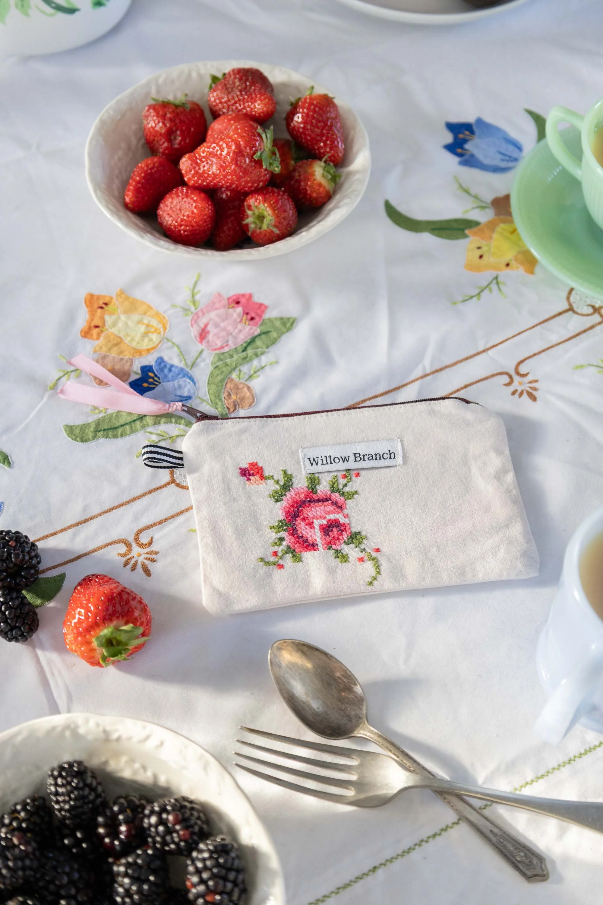 1 Willow Branch general flat pouches laid on vintage table cloth. The pouch is using embroidered vintage napkin on the table is strawberries and blackberries